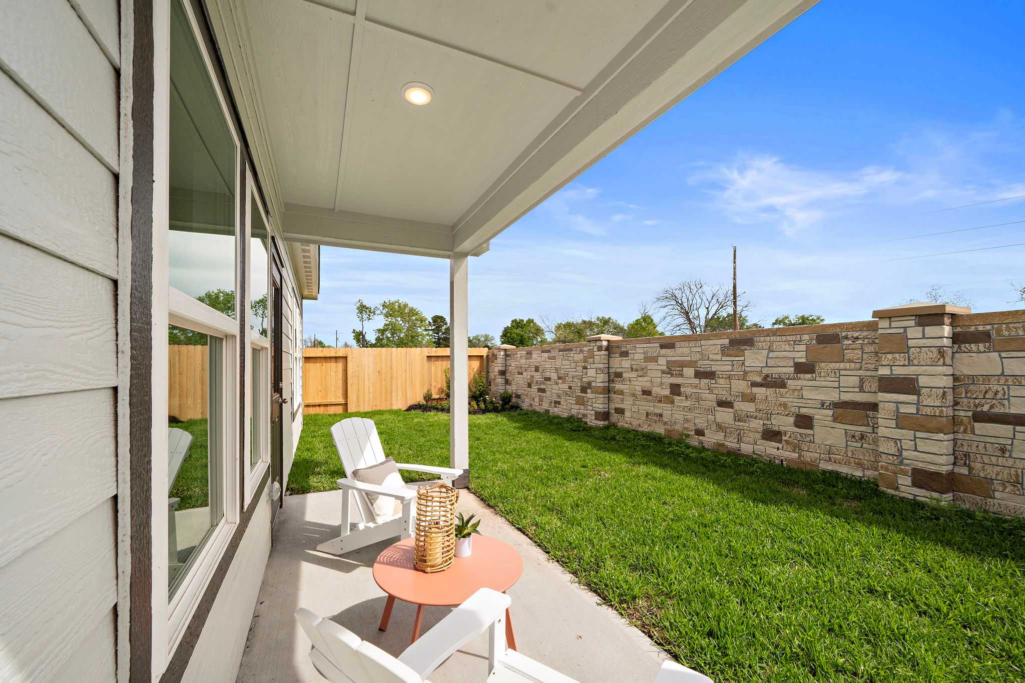 Covered patio at The Villages at WestPointe in Dayton Texas featuring white Adirondack chairs stone wall and lush green lawn by Davidson Homes