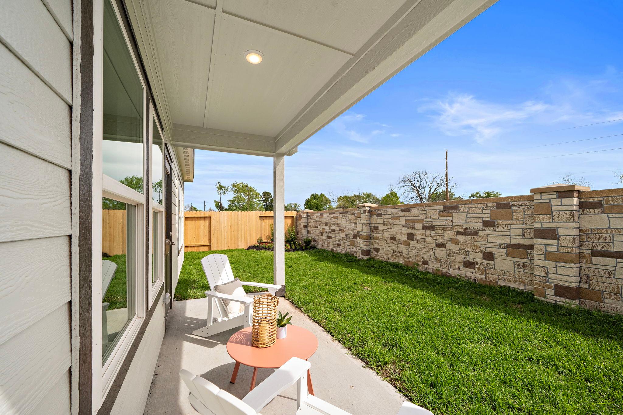 Covered patio at The Villages at WestPointe in Dayton Texas featuring white Adirondack chairs stone wall and lush green lawn by Davidson Homes