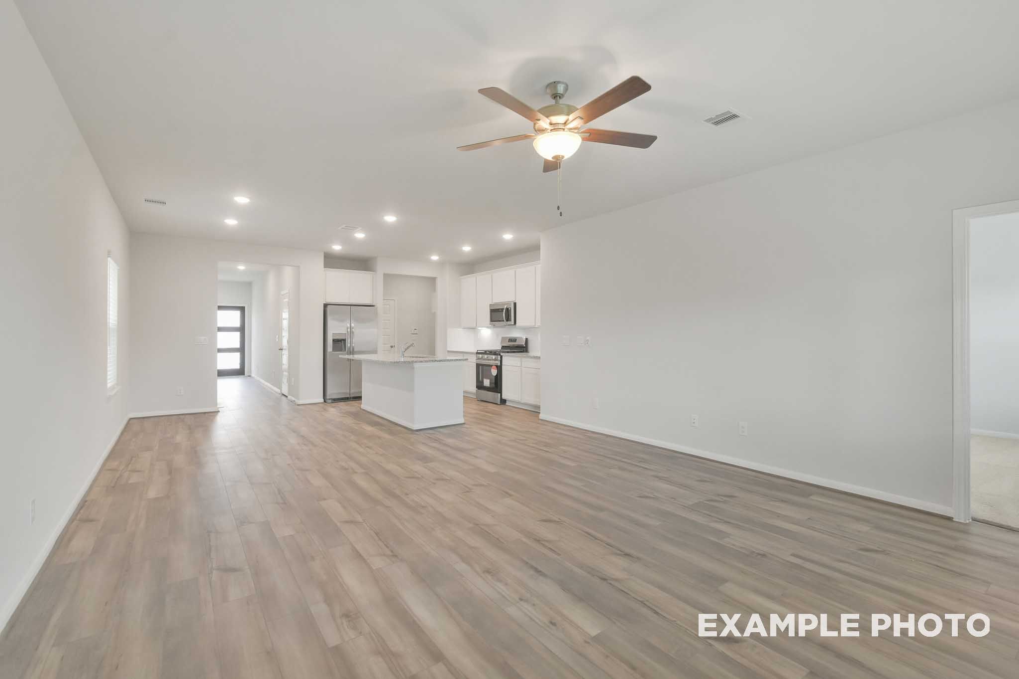 Open-concept living area and kitchen in The Brazos by Davidson Homes featuring wood-look flooring and white cabinetry