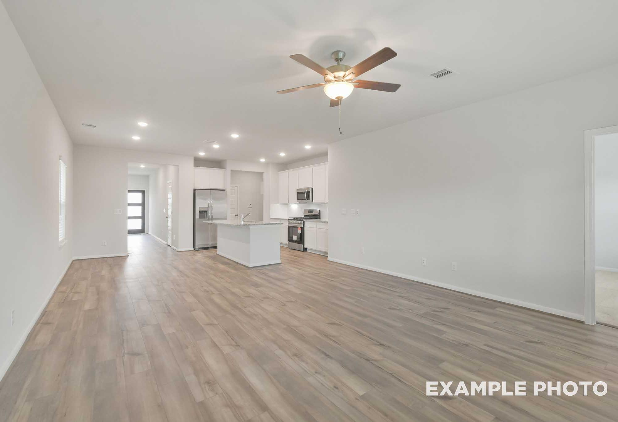 Open-concept living area and kitchen in The Brazos by Davidson Homes featuring wood-look flooring and white cabinetry