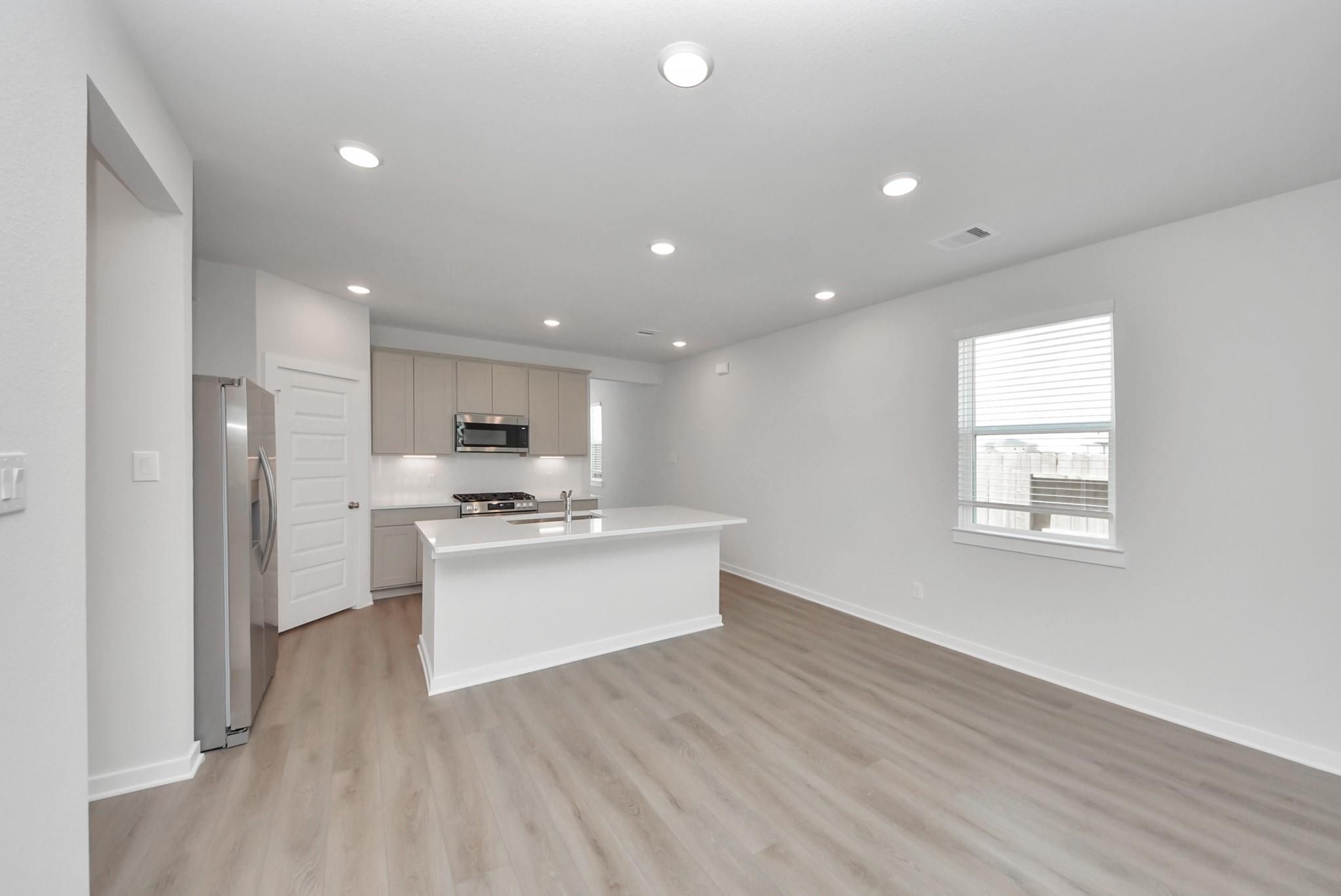 Open-concept kitchen with white island, stainless appliances and wood-look flooring in Davidson Homes The San Marcos E, Beasley, TX