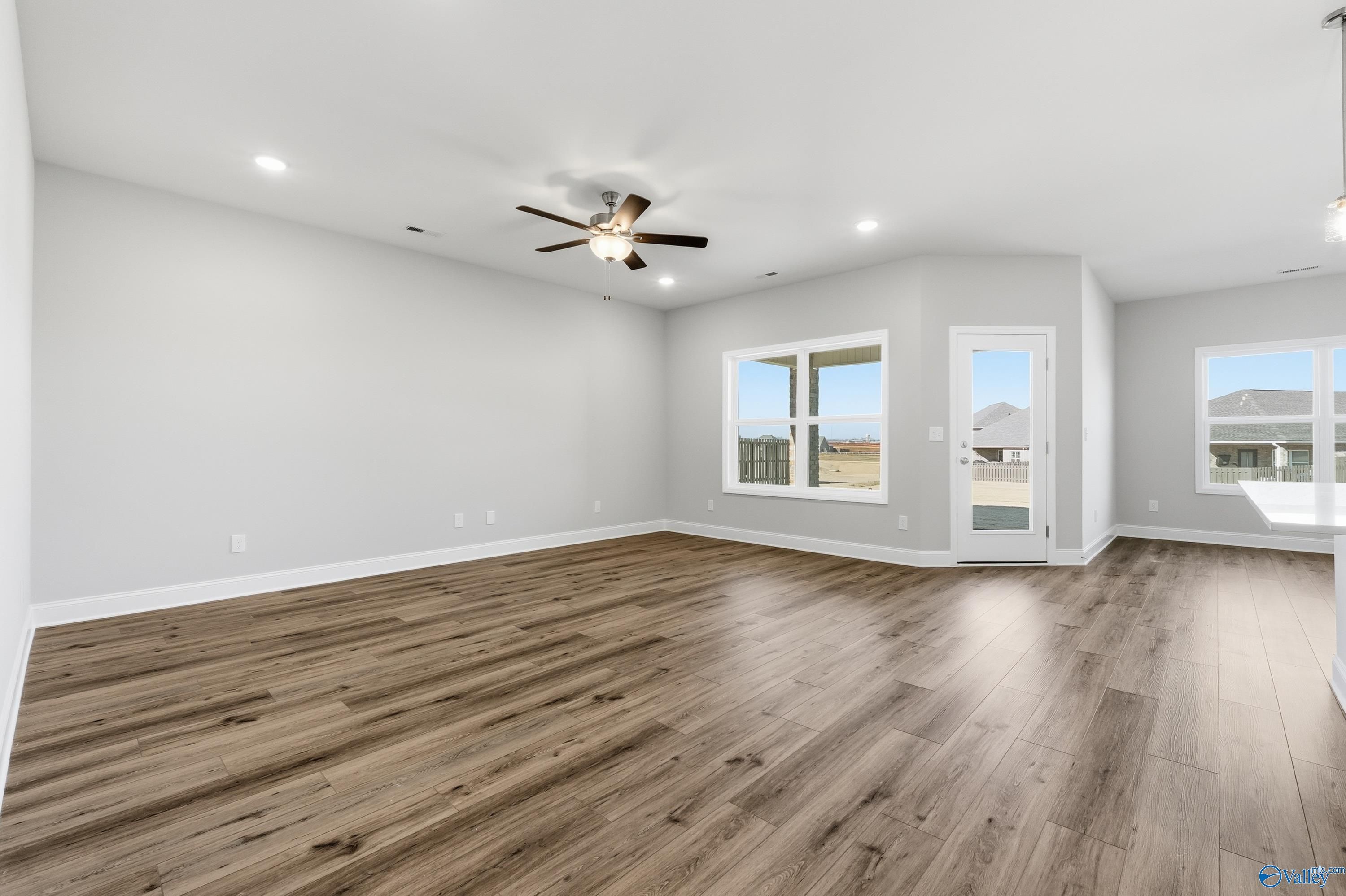 Bright open living room with light gray walls, hardwood floors, ceiling fan, and large windows in Davidson Homes The Everett, Harvest, Alabama