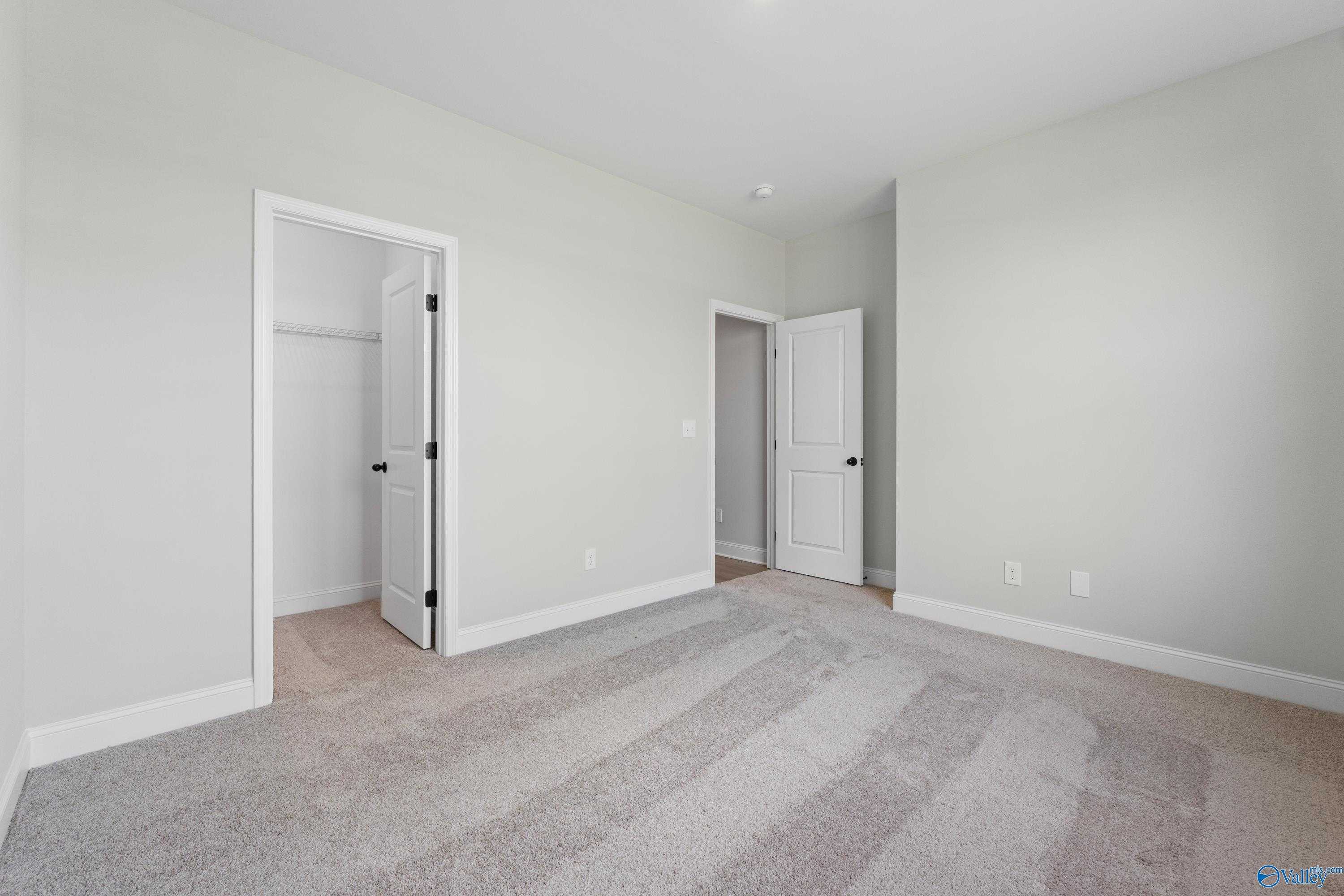 Spacious secondary bedroom with neutral gray walls, carpet flooring, and adjacent closet in Davidson Homes The Rockford, Toney, Alabama