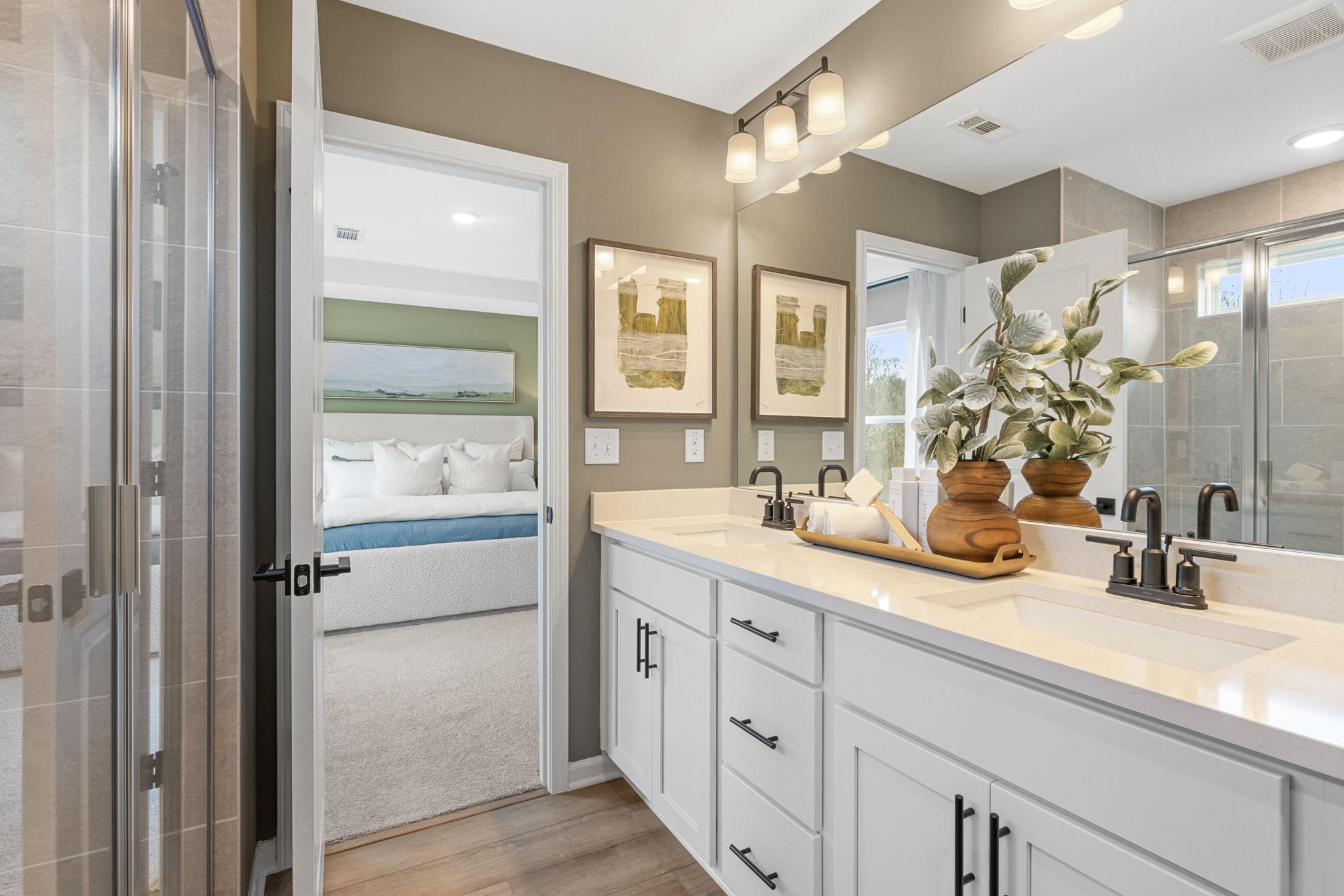 Spacious master bathroom at Links Crossing in Auburn Alabama with double vanity, white cabinets, large mirror, and open bedroom door