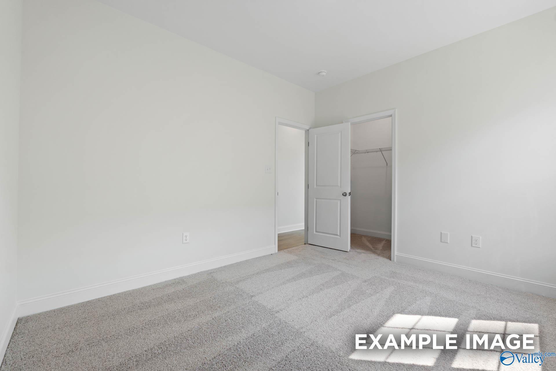 Bright secondary bedroom with neutral carpet, walk-in closet, and white walls in Davidson Homes The Rockford C, Madison, Alabama