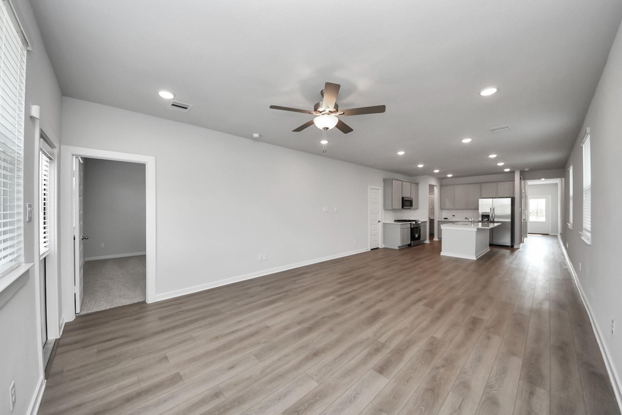 Open-concept living room and kitchen with luxury vinyl plank flooring, ceiling fan, and island in Davidson Homes The Frio F, Houston