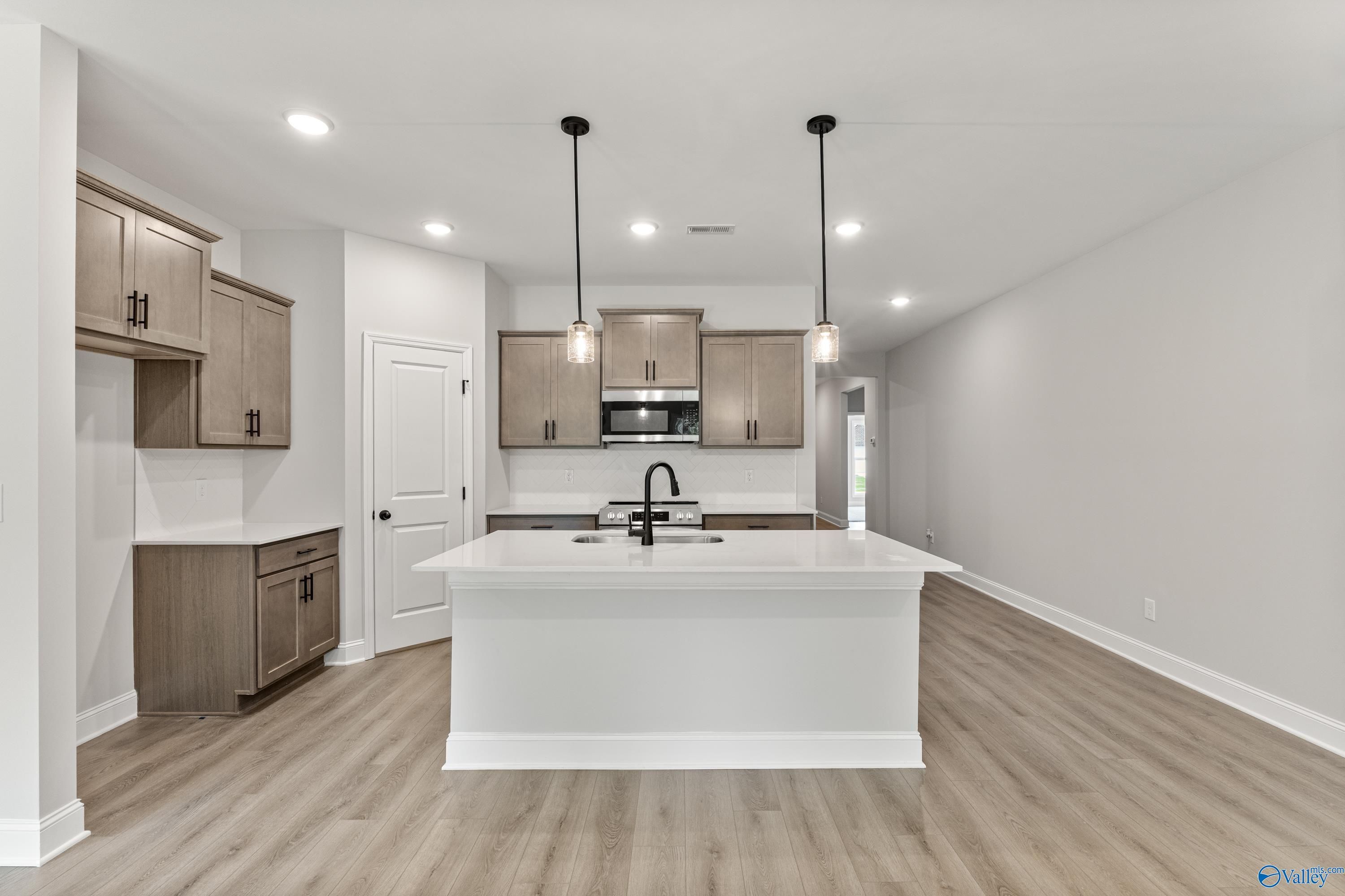 Modern kitchen with white quartz island, light wood cabinets, stainless appliances, and pendant lights in Davidson Homes The Daphne, Huntsville AL