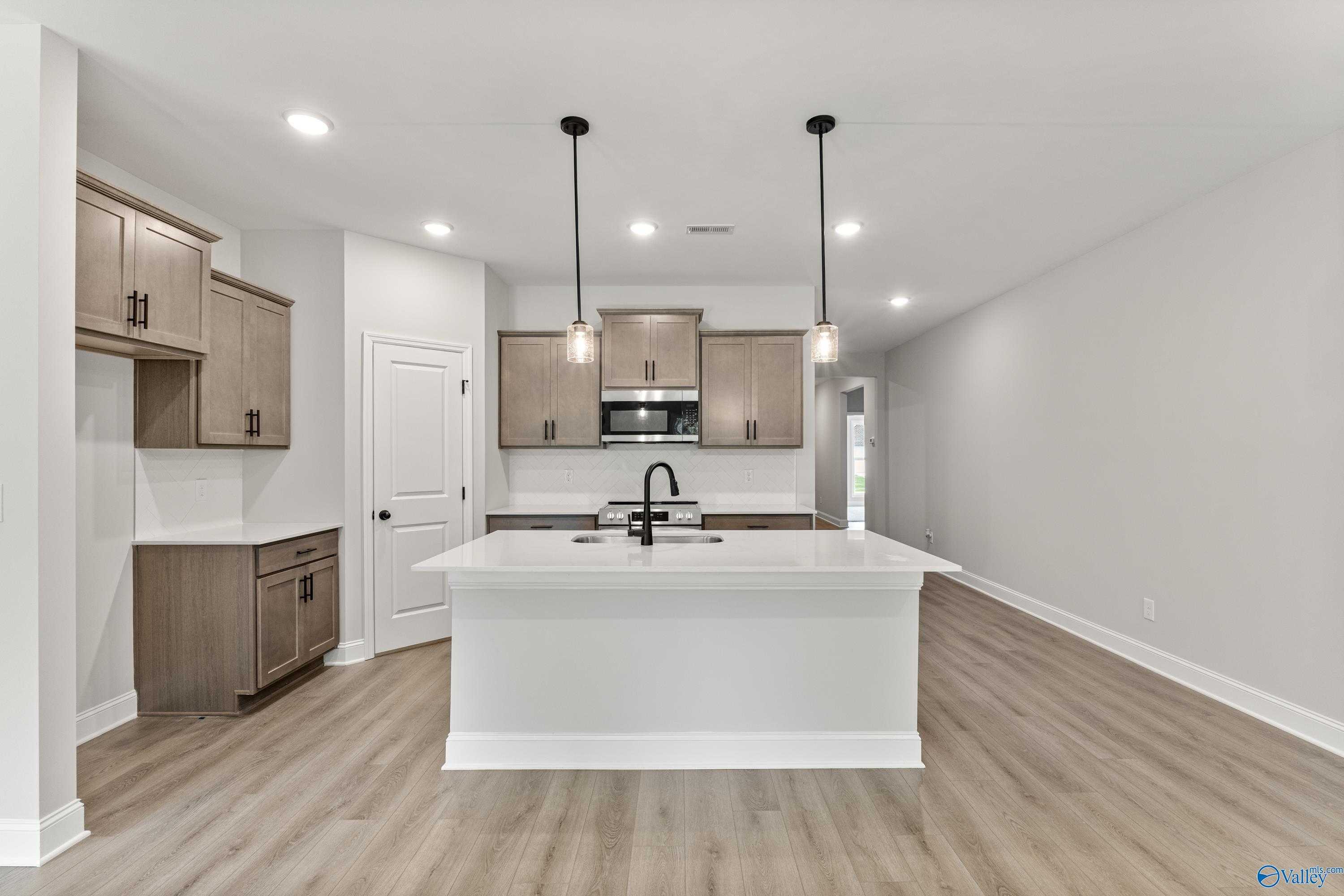 Modern kitchen with white quartz island, light wood cabinets, stainless appliances, and pendant lights in Davidson Homes The Daphne, Huntsville AL