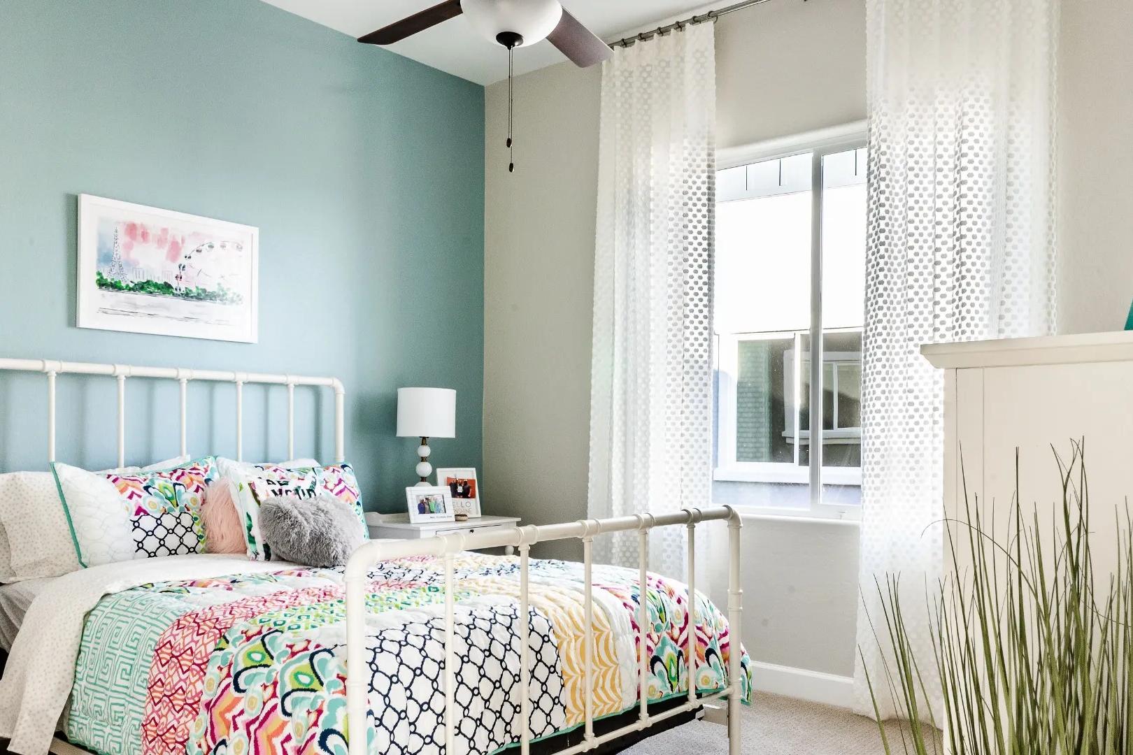 Cozy bedroom interior at Westwood in Prescott AZ by Davidson Homes with colorful bedding, blue walls and sheer curtains