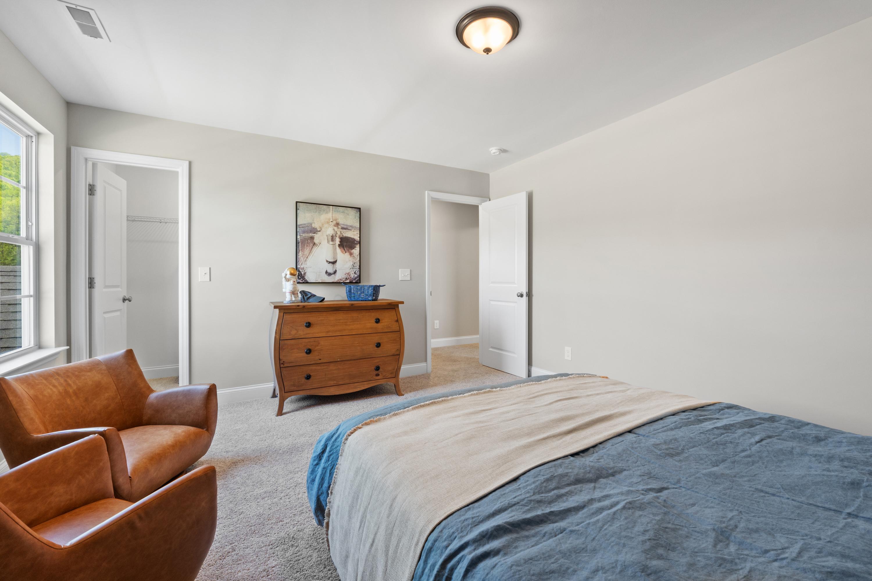 Spacious master bedroom in The Haven D featuring wooden dresser, cow artwork, leather armchairs, and blue linens