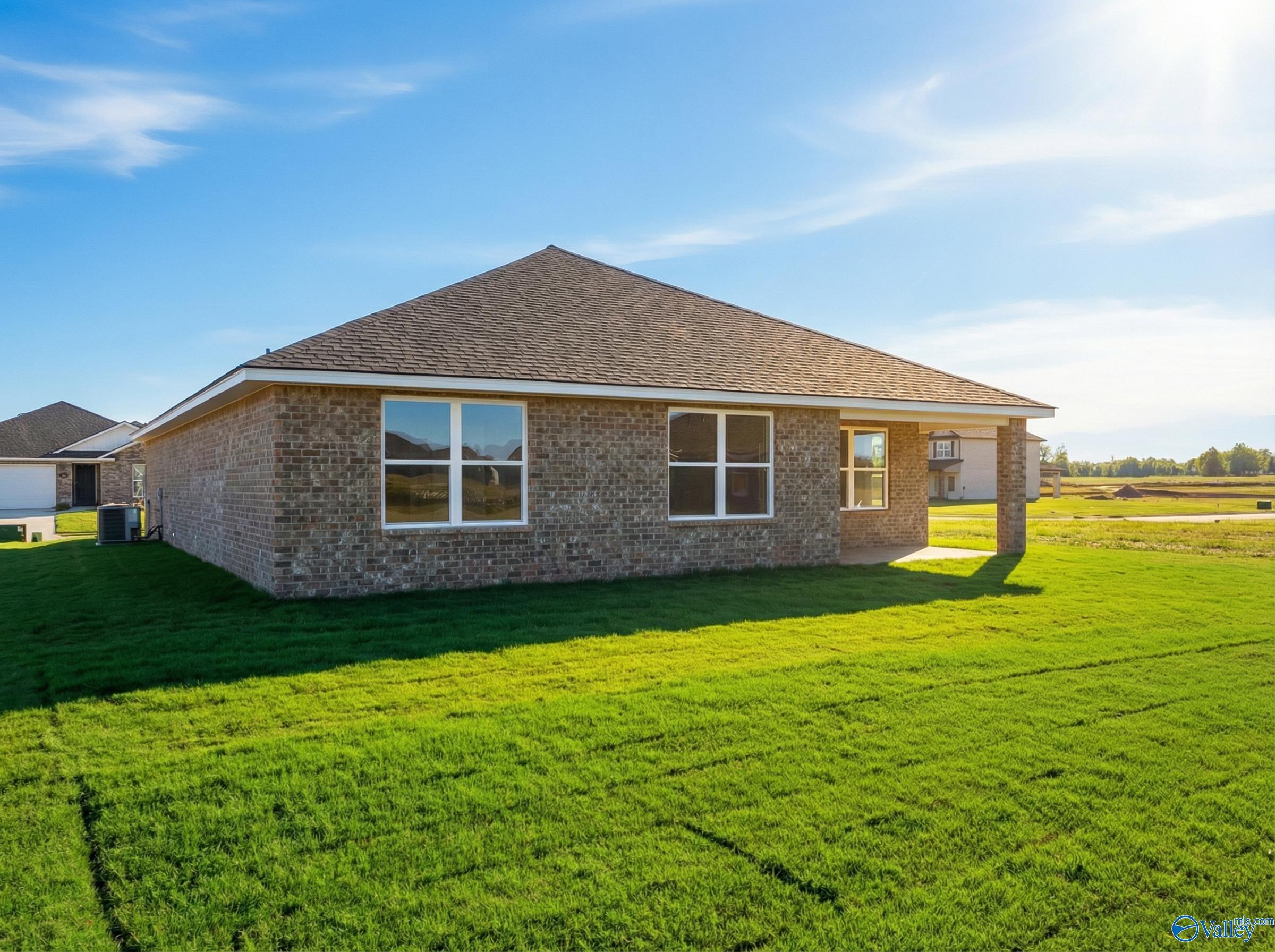 Side view of The Franklin 3-bedroom brick home with gabled roof, large windows, and attached garage on lush green lawn in Heritage Lakes, New Market, Alabama