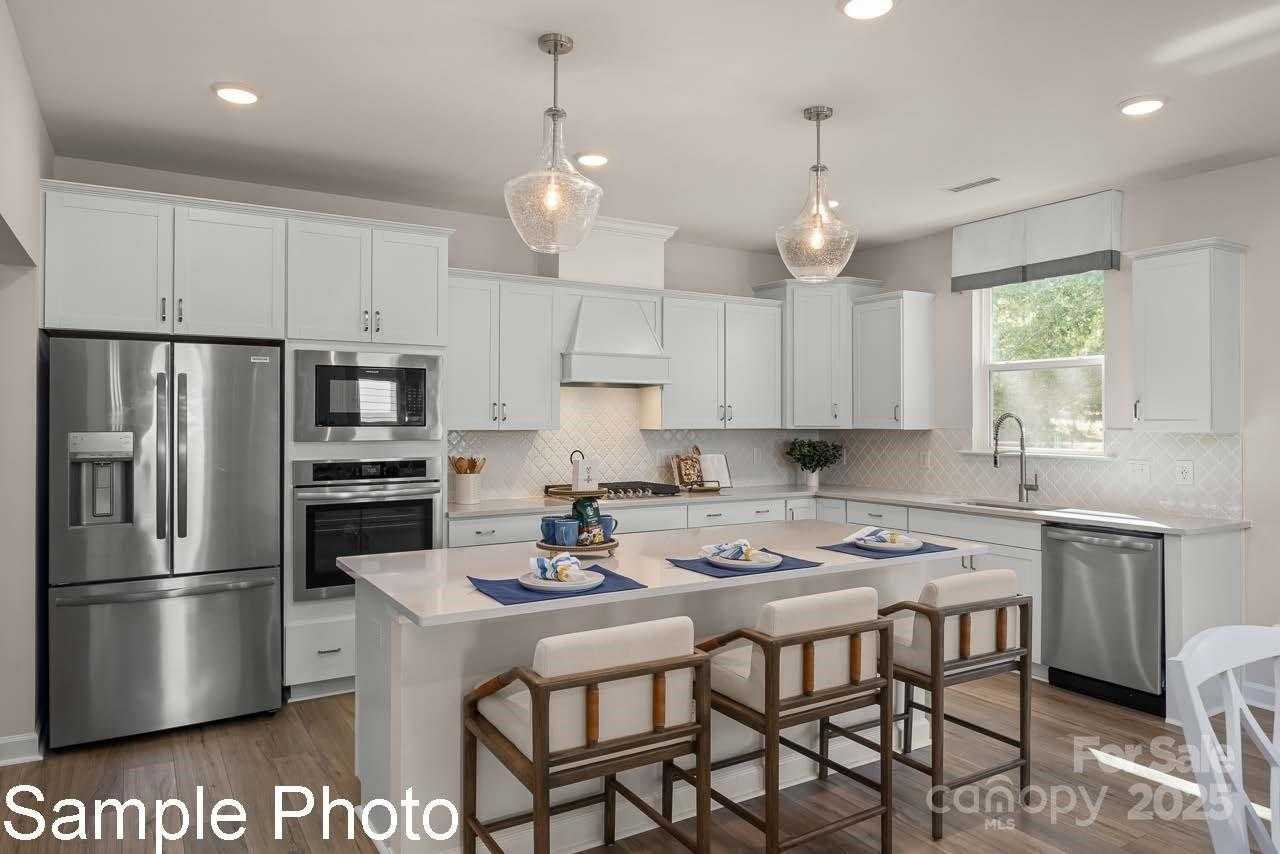 Modern white kitchen with quartz island, stainless appliances, pendant lights in Davidson Homes Hickory E II, Belmont, NC