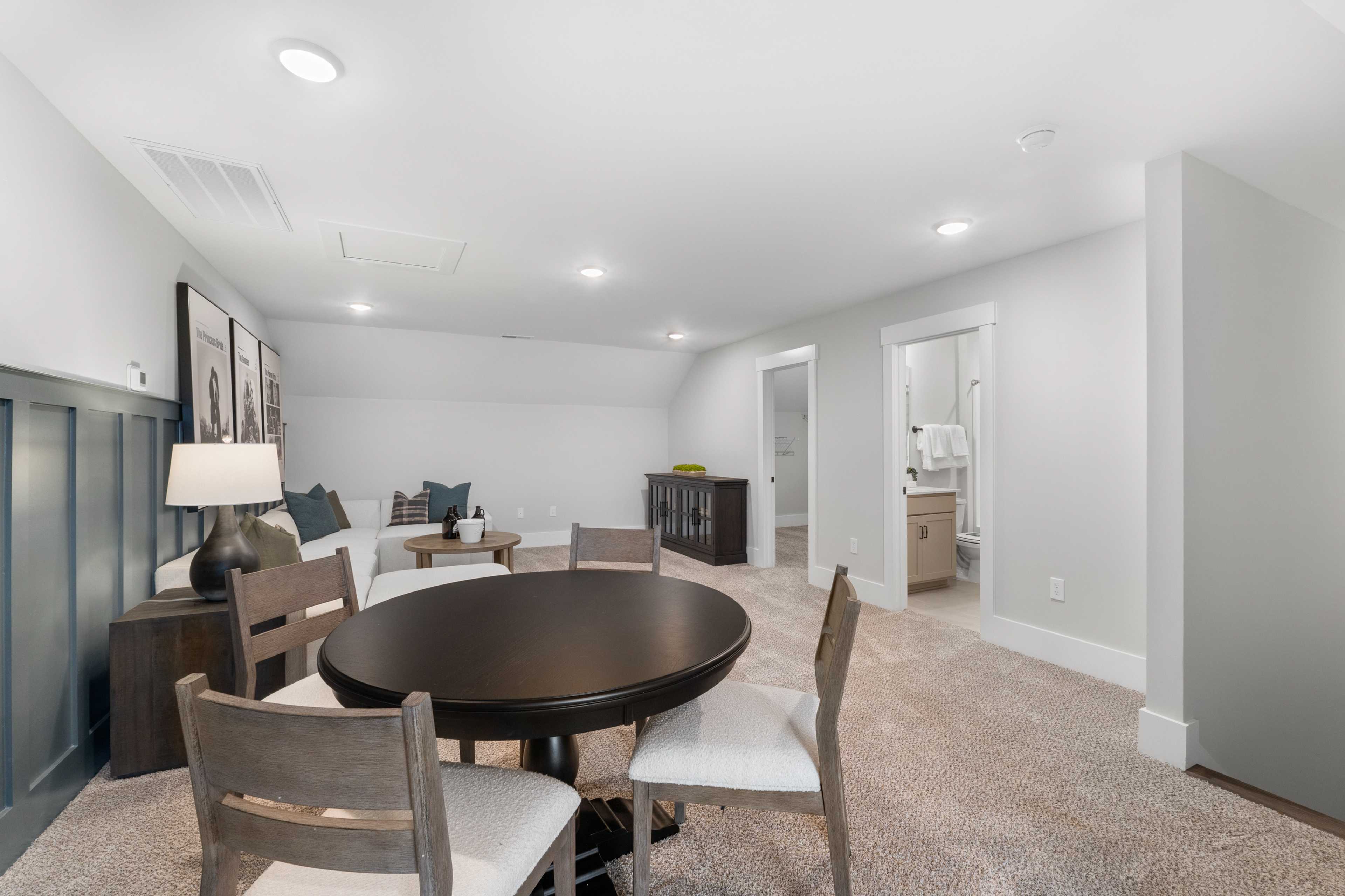 Spacious bonus room at Kendall Farms in Toney AL with round wood table, upholstered chairs, couch, and open bathroom access