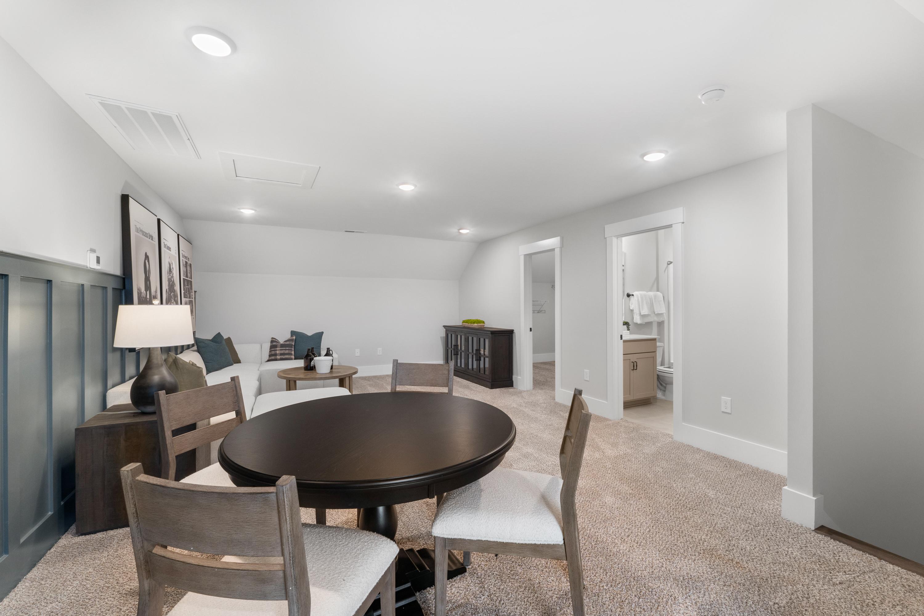 Spacious bonus room at Kendall Farms in Toney AL with round wood table, upholstered chairs, couch, and open bathroom access