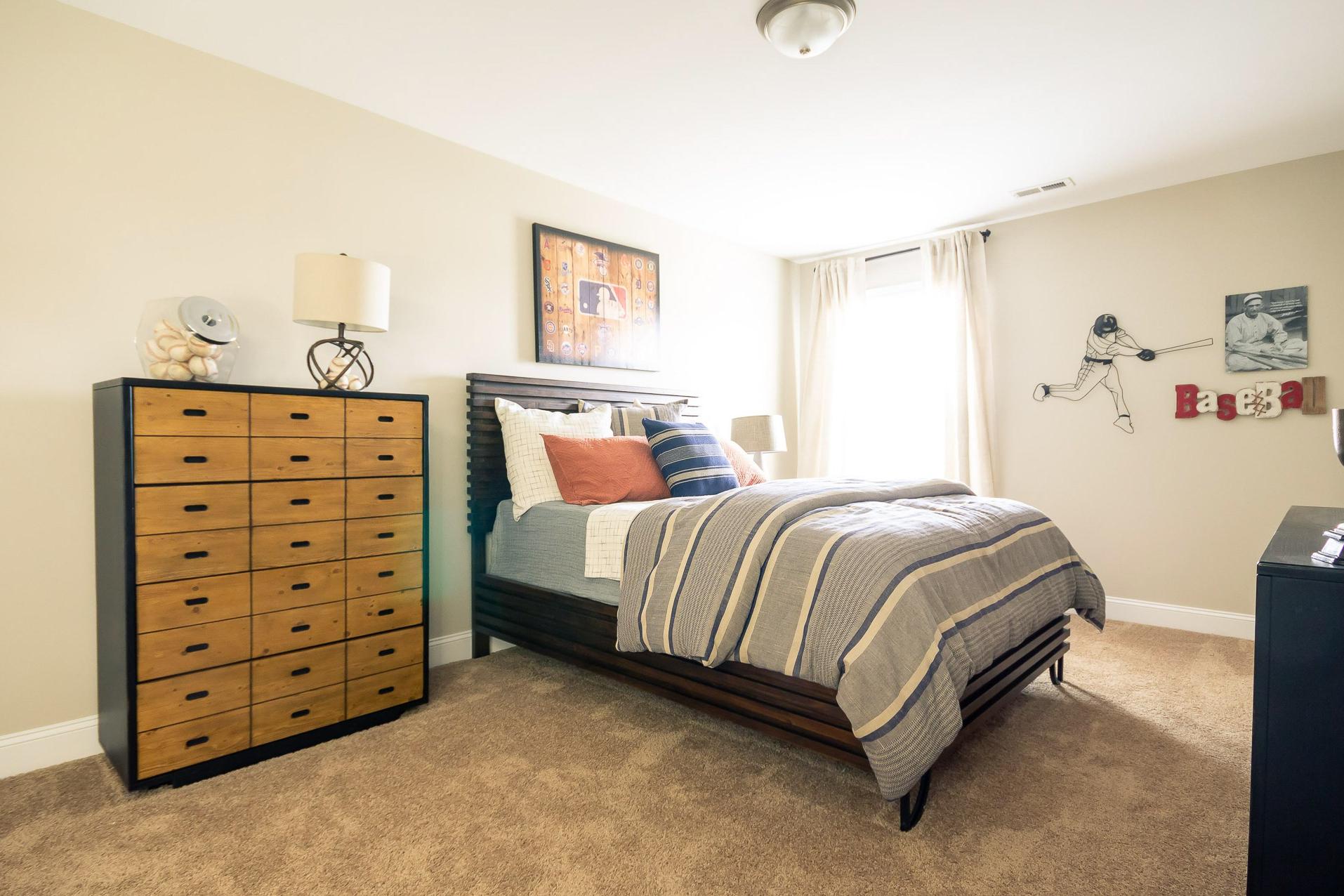 Cozy boy's bedroom at Summer Pointe in Madison Alabama with baseball wall decor, striped bedding, and tall wooden dresser