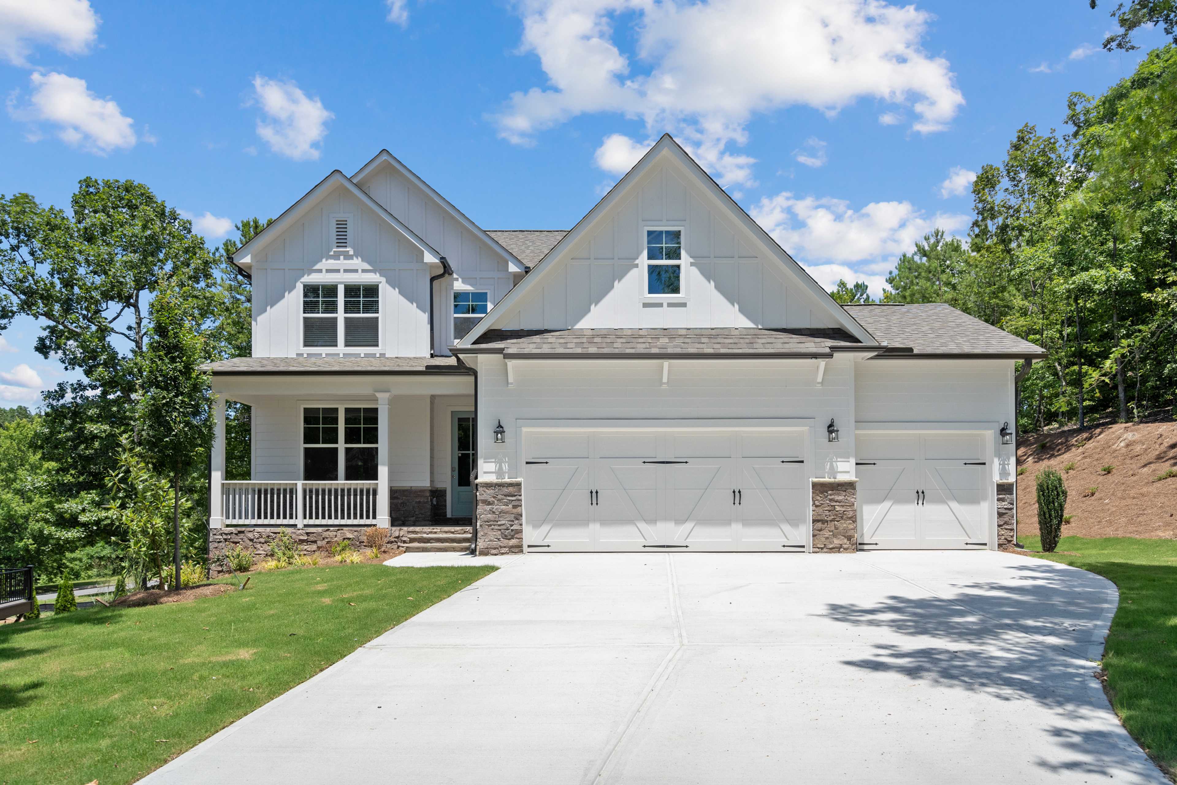 Modern farmhouse home exterior at Mountainbrook in Cartersville GA with white siding, covered porch, two-car garage and lush landscaping