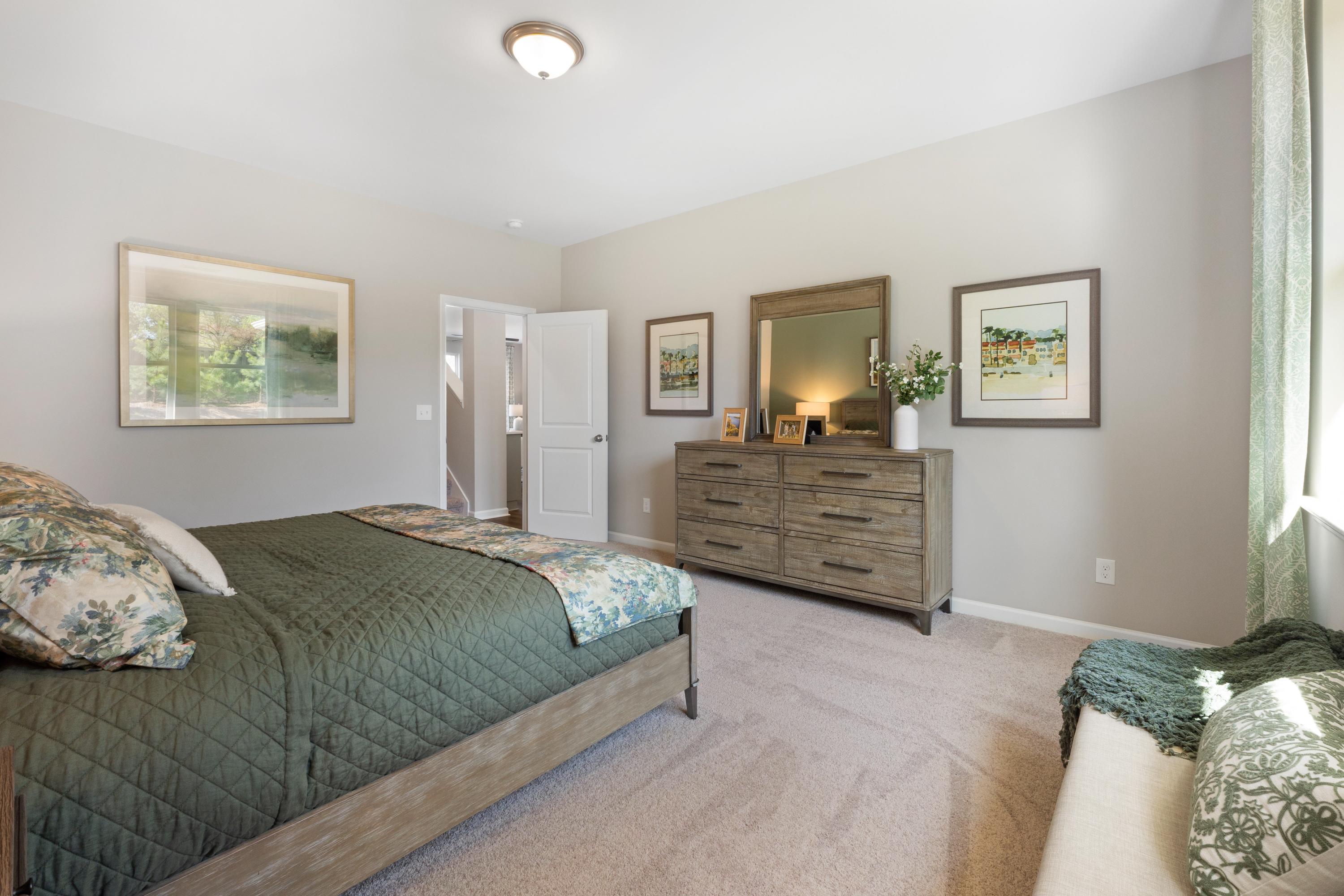 Spacious bedroom at Evergreen Mill in Madison, AL with wooden bed frame, green floral bedding, mirrored dresser, and wall art
