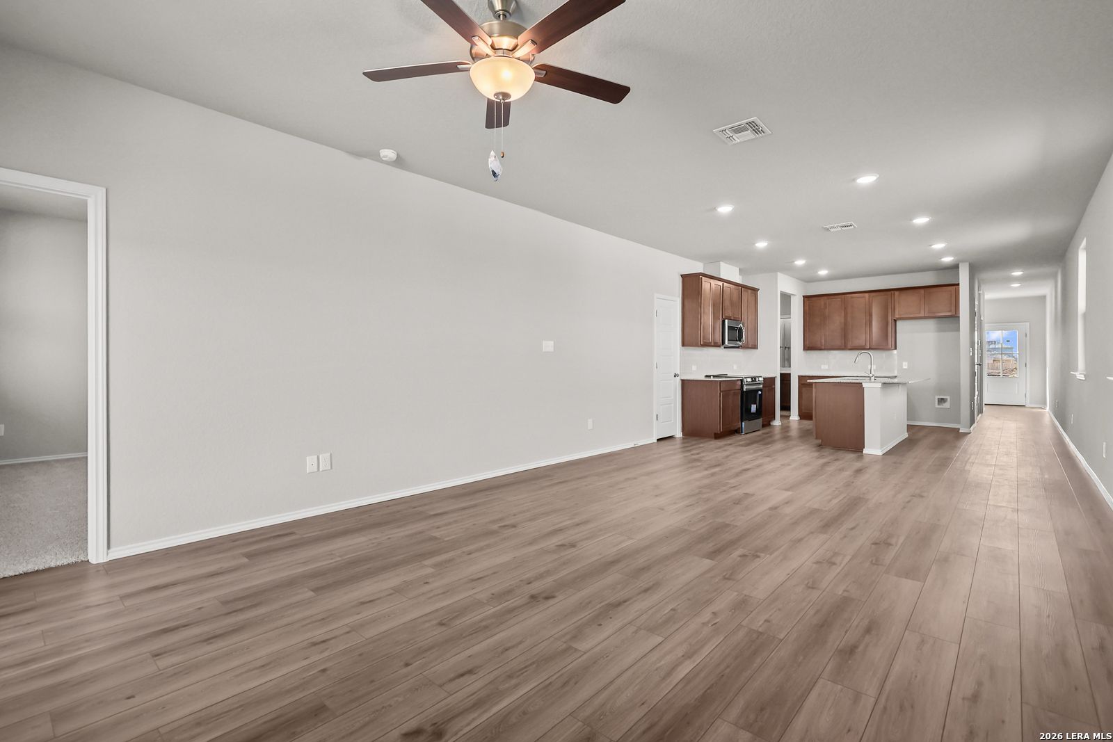 Spacious open living and kitchen area with white cabinets, island, stainless appliances, and ceiling fan in Davidson Homes The Frio B, San Antonio