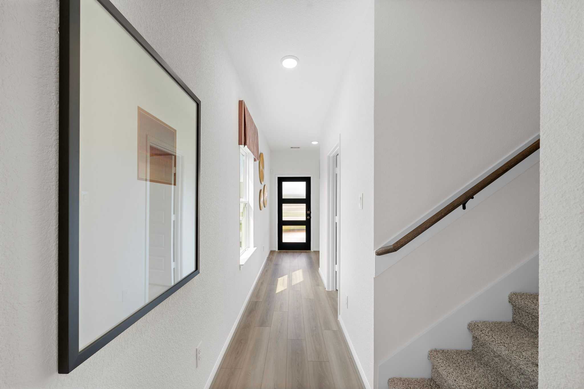 Spacious white hallway with light wood floors, large framed mirror, and carpeted staircase at The Villages at WestPointe in Dayton Texas