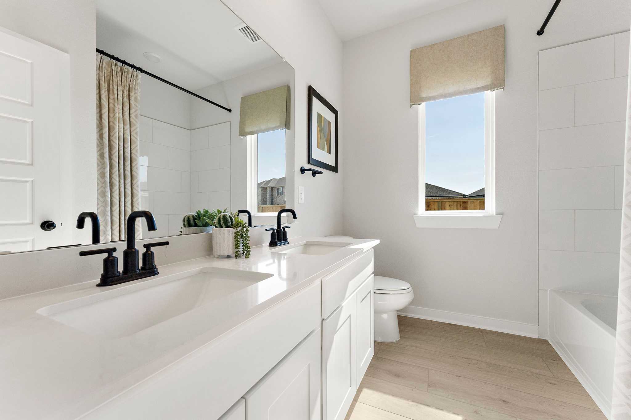 Modern white bathroom in Sundance Cove, Crosby Texas with double vanity, black faucets, bathtub, and light wood floors