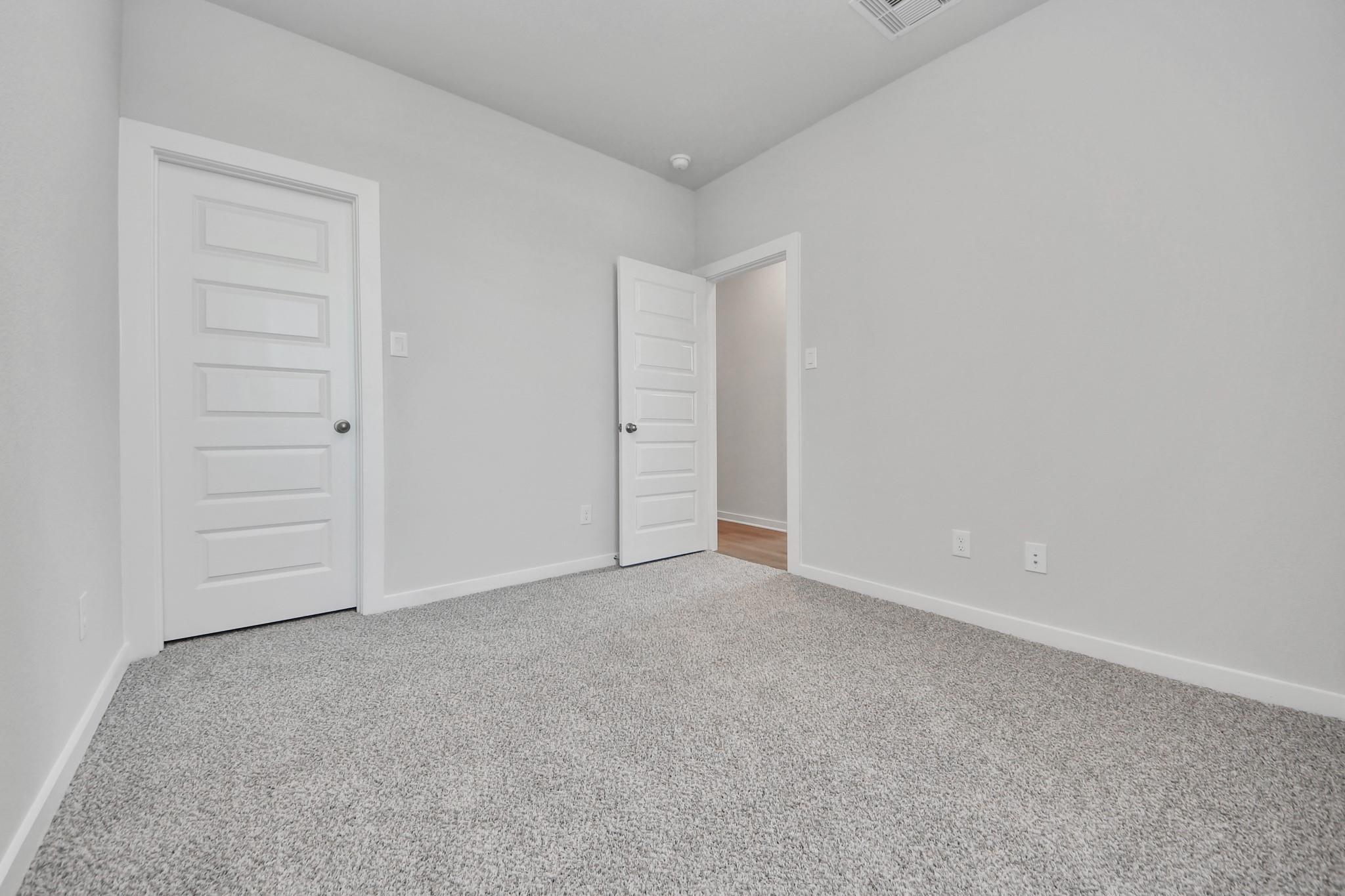 Neutral-toned secondary bedroom with gray carpet and white doors in The Colorado G floor plan by Davidson Homes in Emberly.
