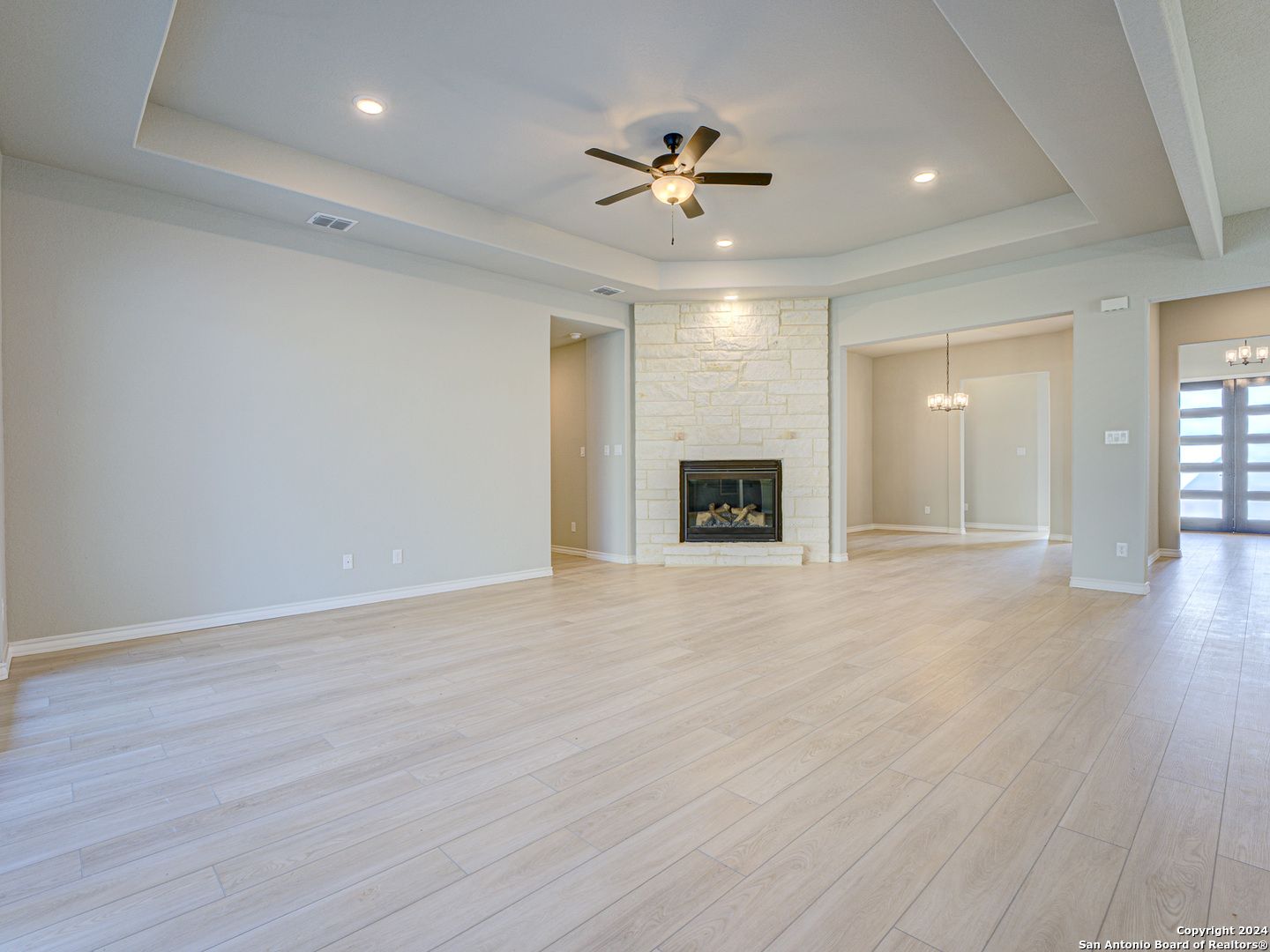 Spacious living room with stone gas fireplace, ceiling fan, and hardwood floors in Davidson Homes The Summerlin A, Castroville, Texas