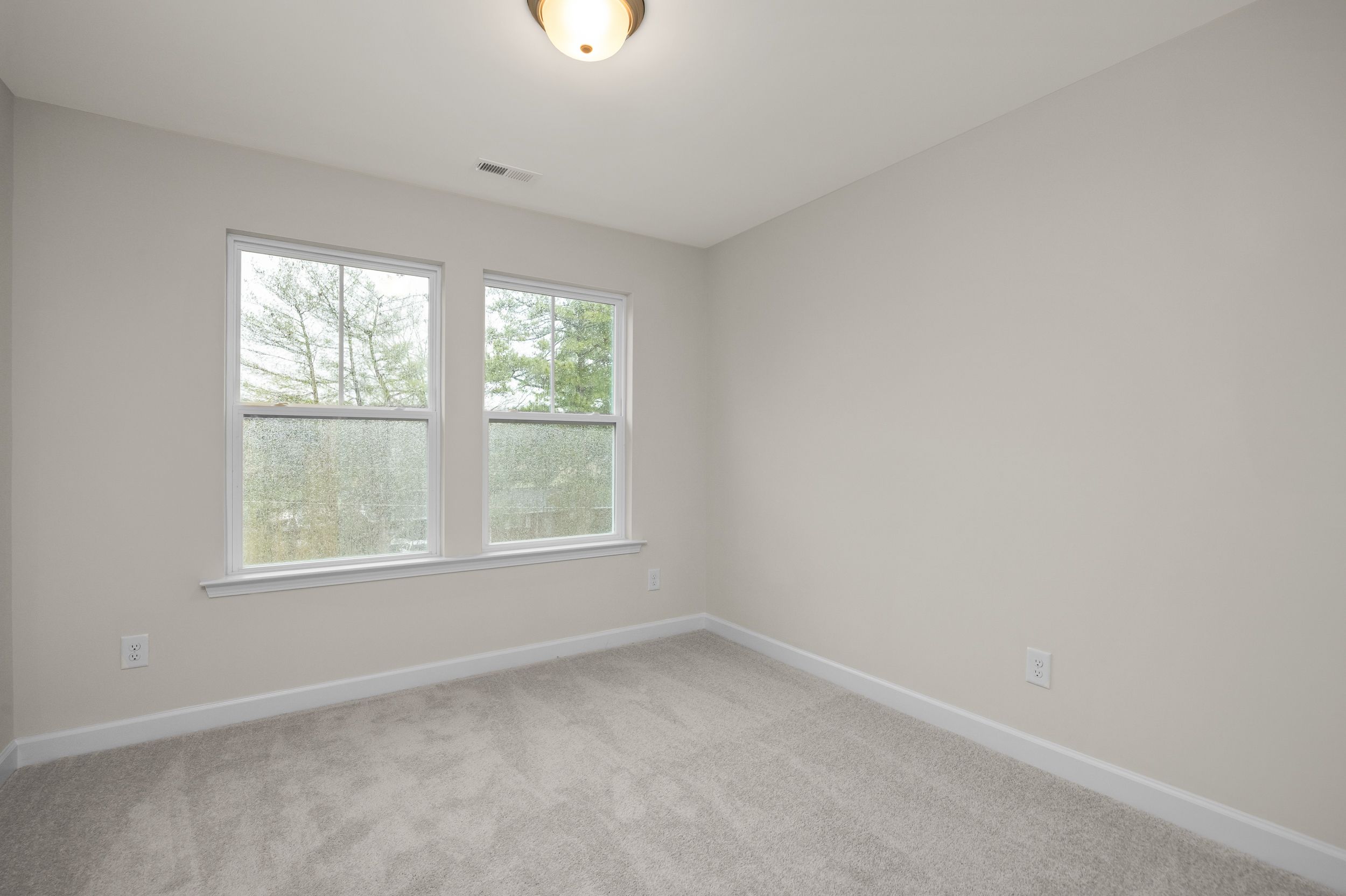 Spacious bedroom interior at Forestville Yard Townhomes in Knightdale NC with gray walls, carpet flooring, and large windows overlooking woods