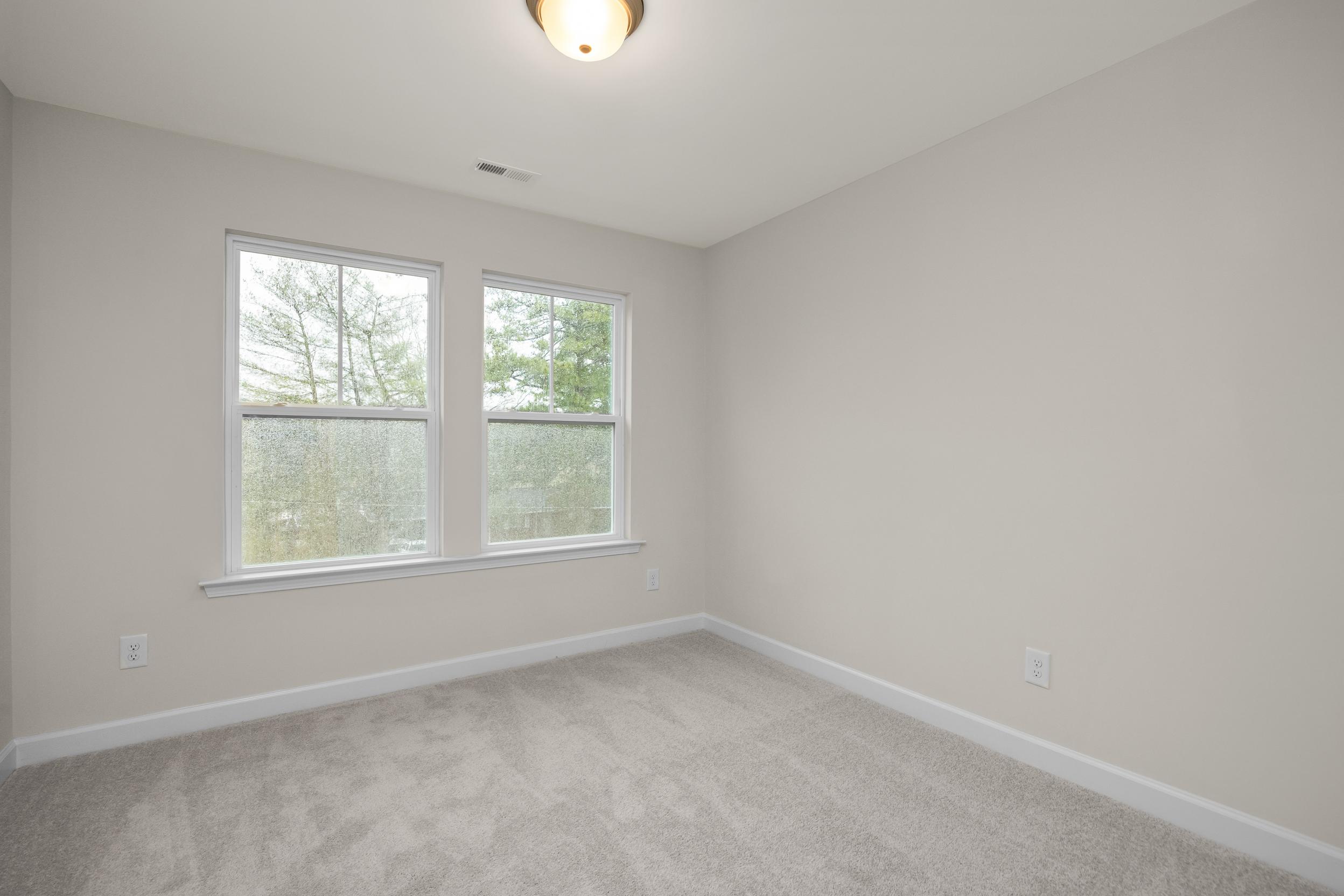 Spacious bedroom interior at Forestville Yard Townhomes in Knightdale NC with gray walls, carpet flooring, and large windows overlooking woods