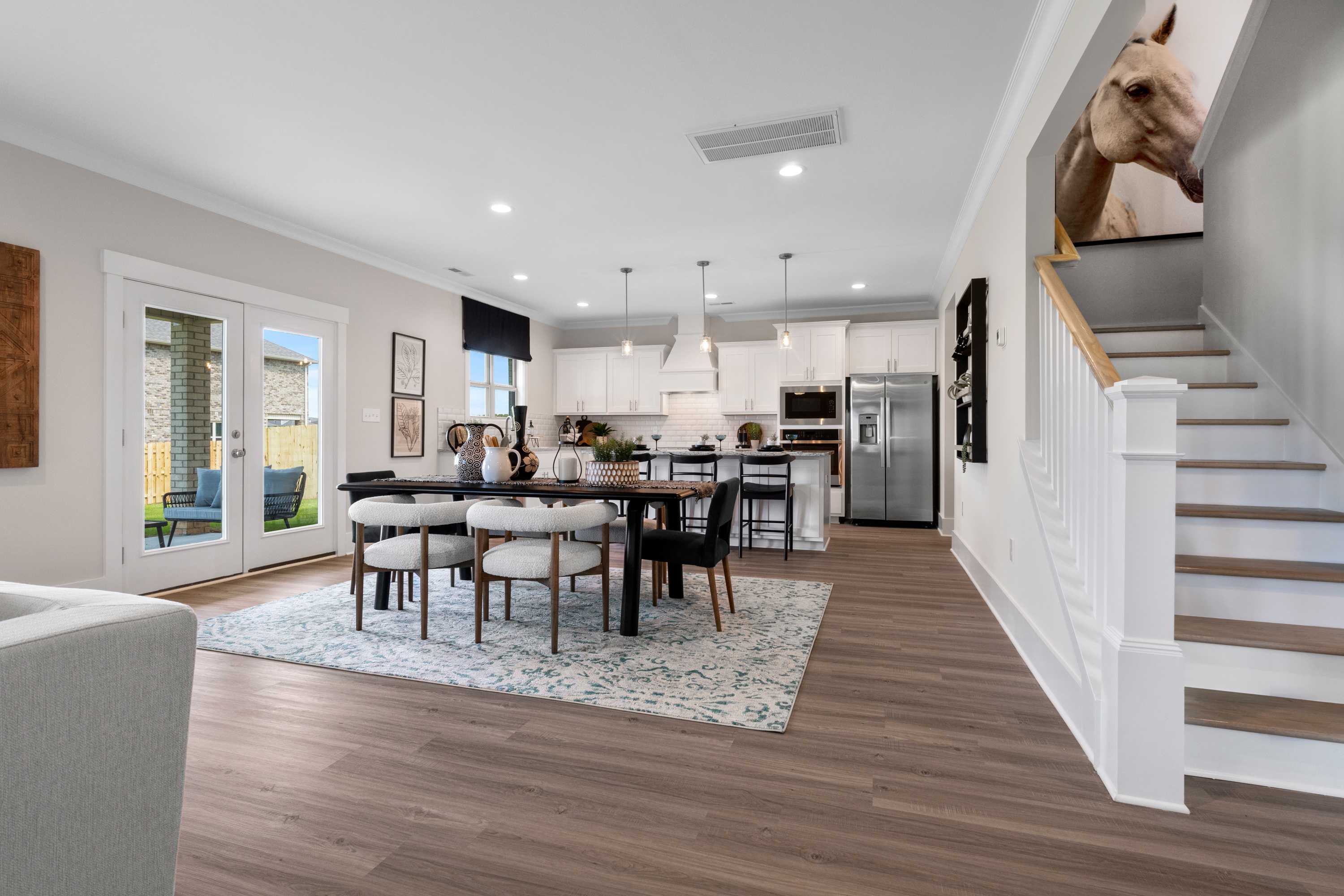 Open-concept kitchen and dining area in The Chelsea A featuring large island, rectangular table with chairs, stainless steel fridge, hardwood floors, and open staircase