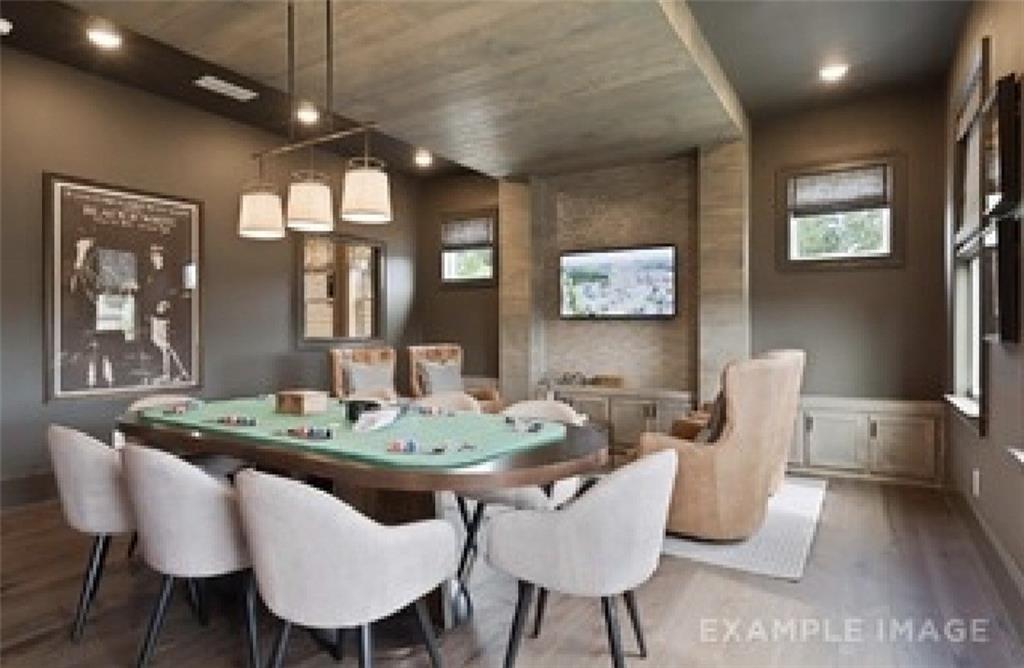 Elegant game room with oval poker table, white chairs, mounted TV, and brick wall in Davidson Homes The Seaside A, Woodstock, GA