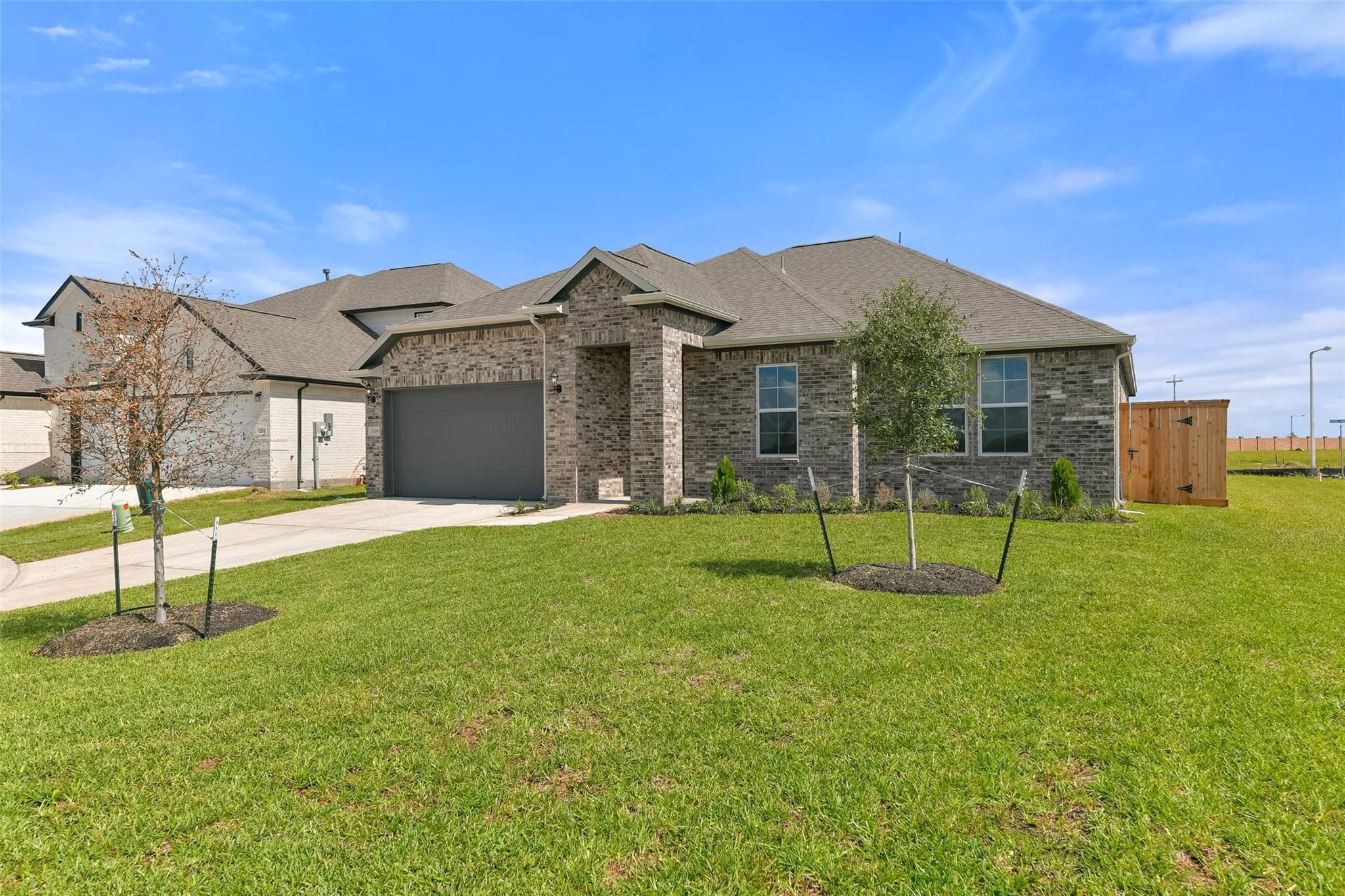 Modern brick and stone single-story home with 2-car garage, landscaped front yard, and young trees in Lago Mar, Texas City by Davidson Homes
