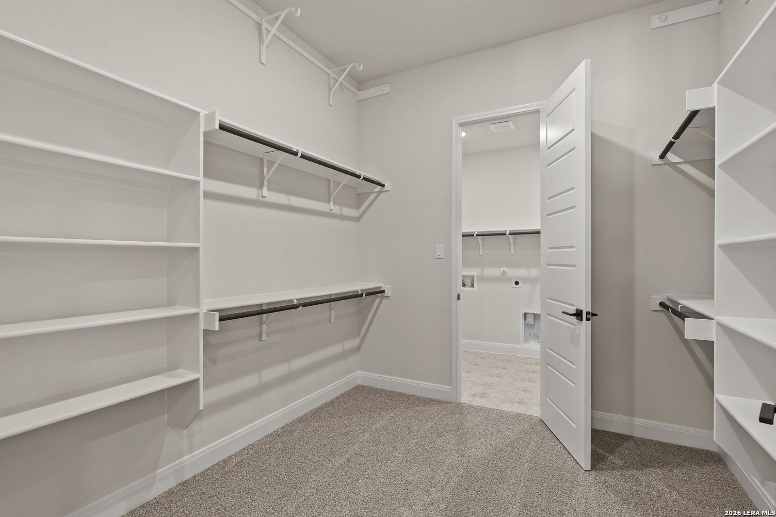 Walk-in closet with built-in shelving connecting to the laundry room in The Summerlin B home, Potranco Oaks, Castroville.