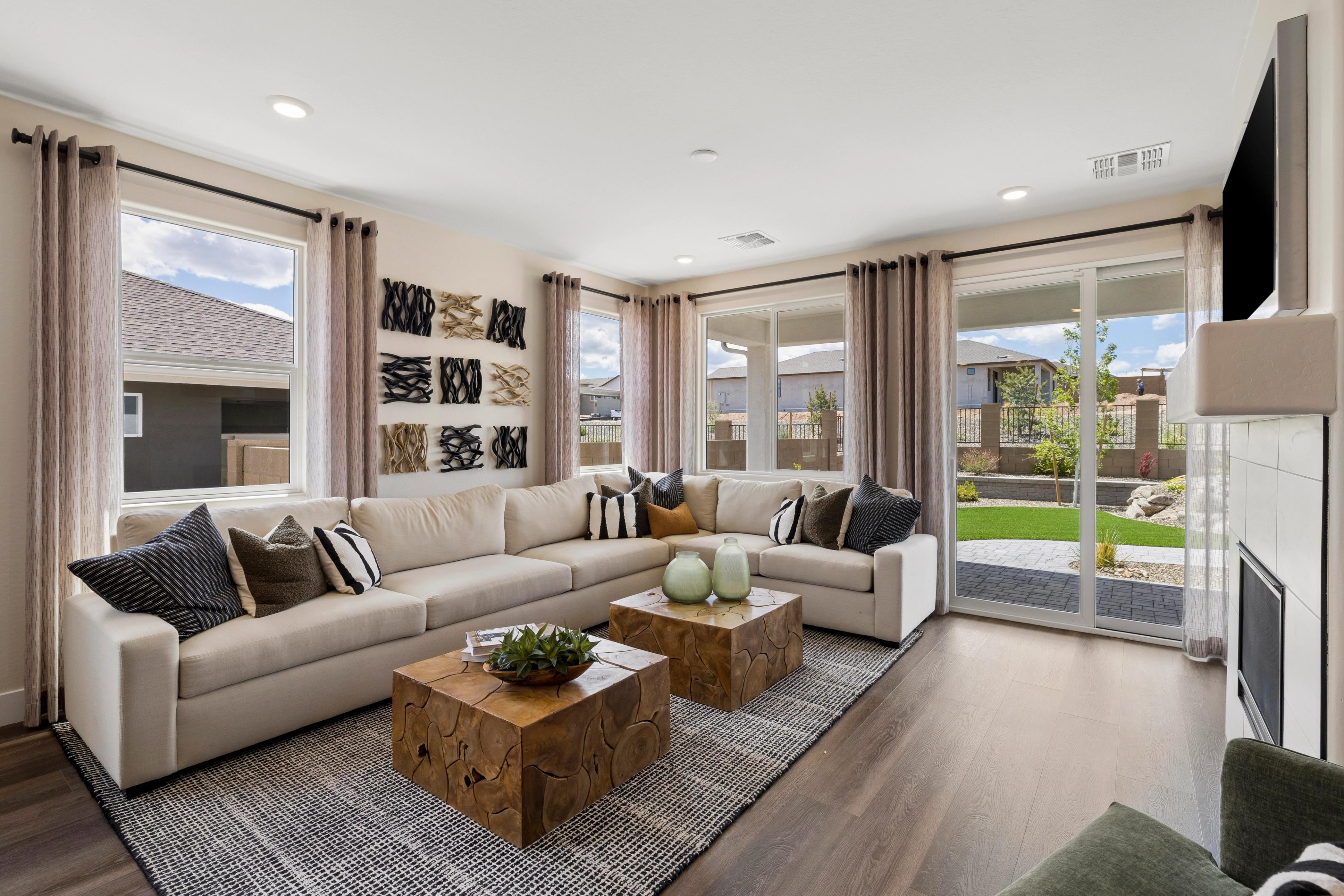 Spacious living room at South Ranch Western Collection in Prescott AZ with beige L-shaped sofa, wooden tables, and sliding doors to green backyard