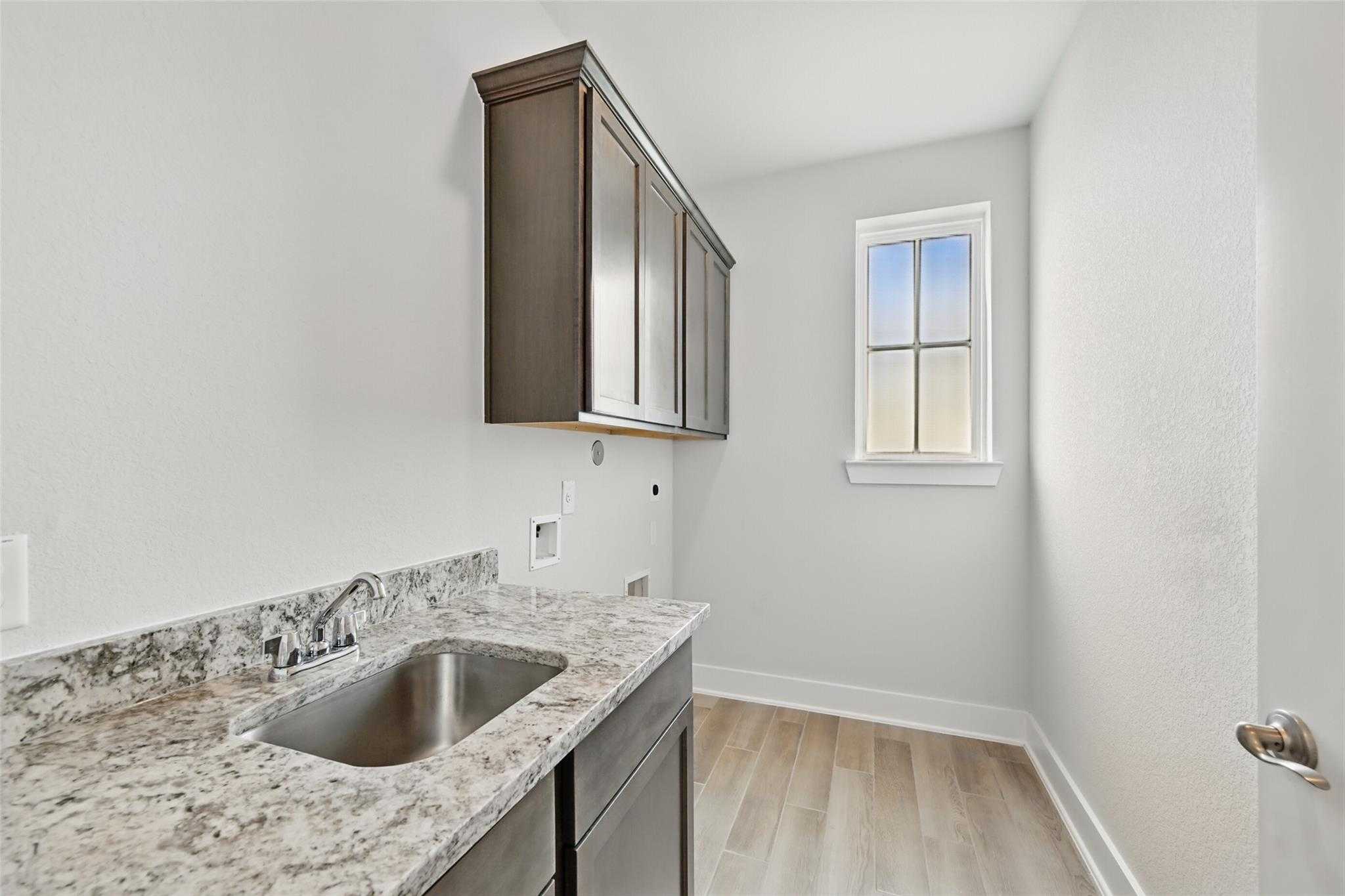 Modern laundry room featuring granite utility sink, dark wood cabinets, and window in Davidson Homes The Philip A, Lago Mar, Texas City
