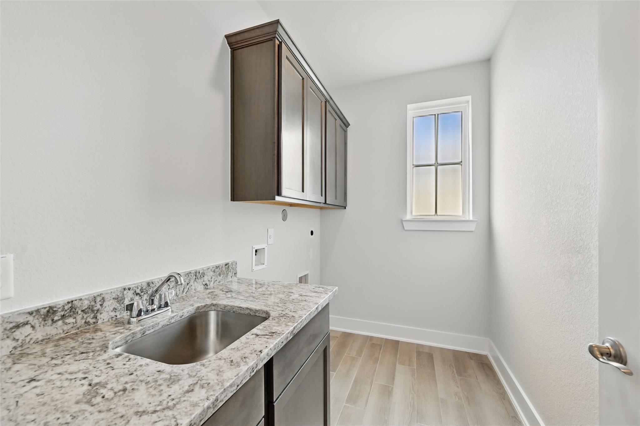 Modern laundry room featuring granite utility sink, dark wood cabinets, and window in Davidson Homes The Philip A, Lago Mar, Texas City