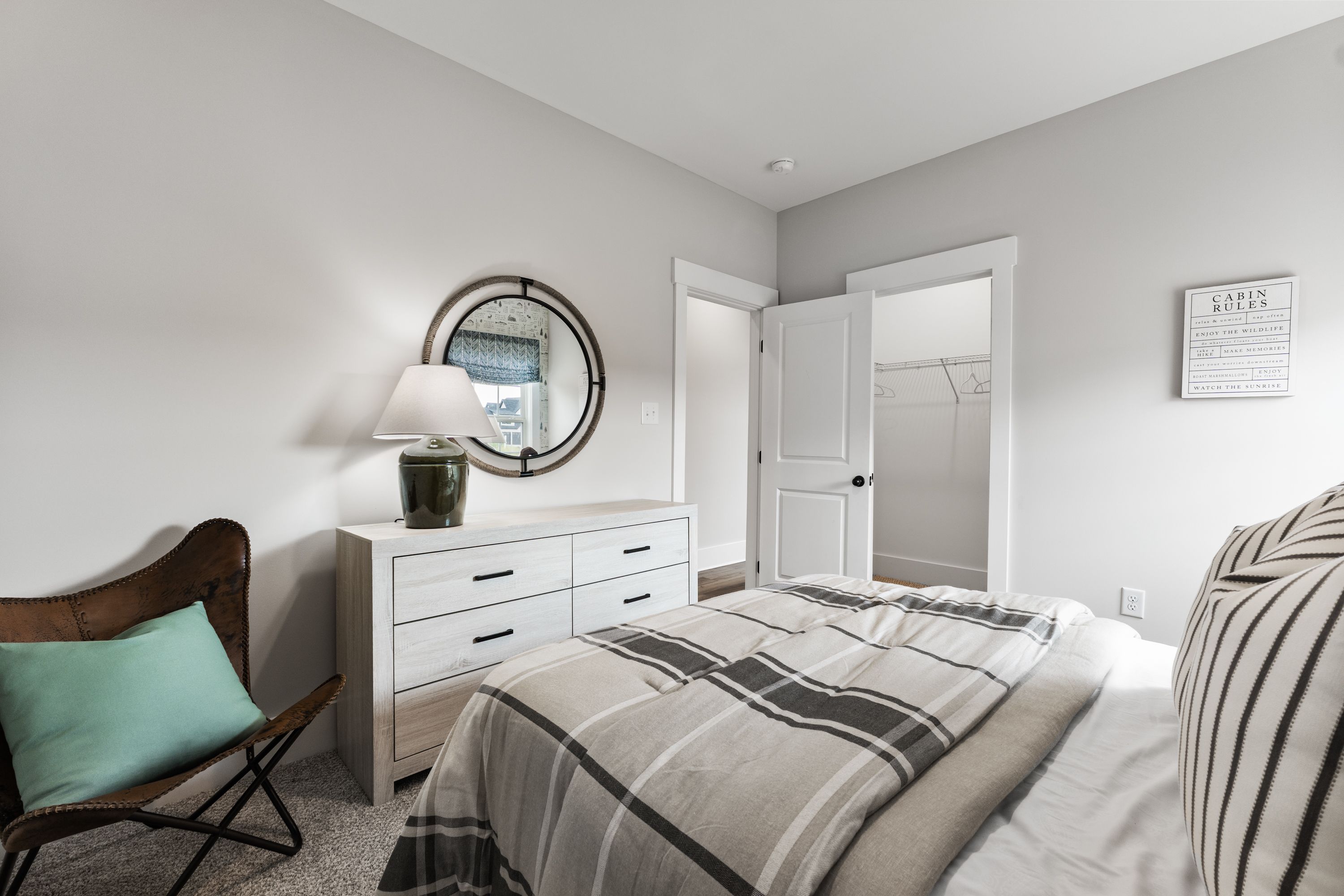Cozy bedroom interior at River Road Estates in Decatur, Alabama with white dresser, round mirror, plaid bedding, and leather chair