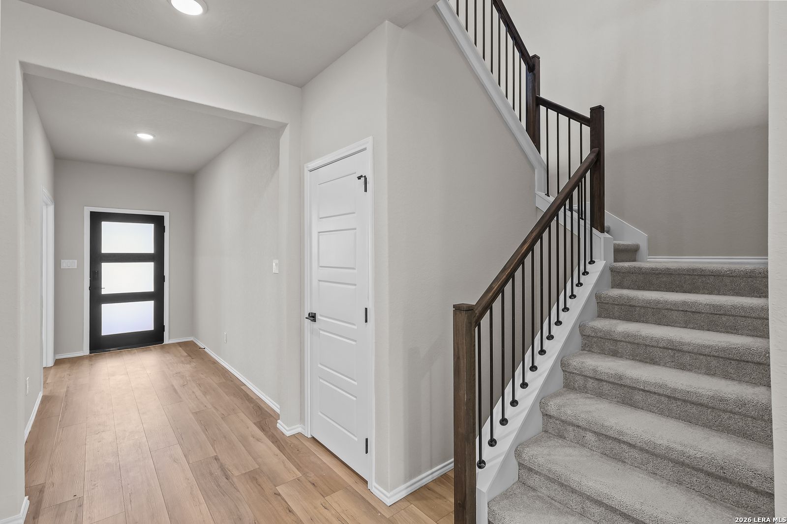 Bright entryway with wood-look flooring, black front door, and carpeted staircase in Davidson Homes' The Sequoia C, San Antonio