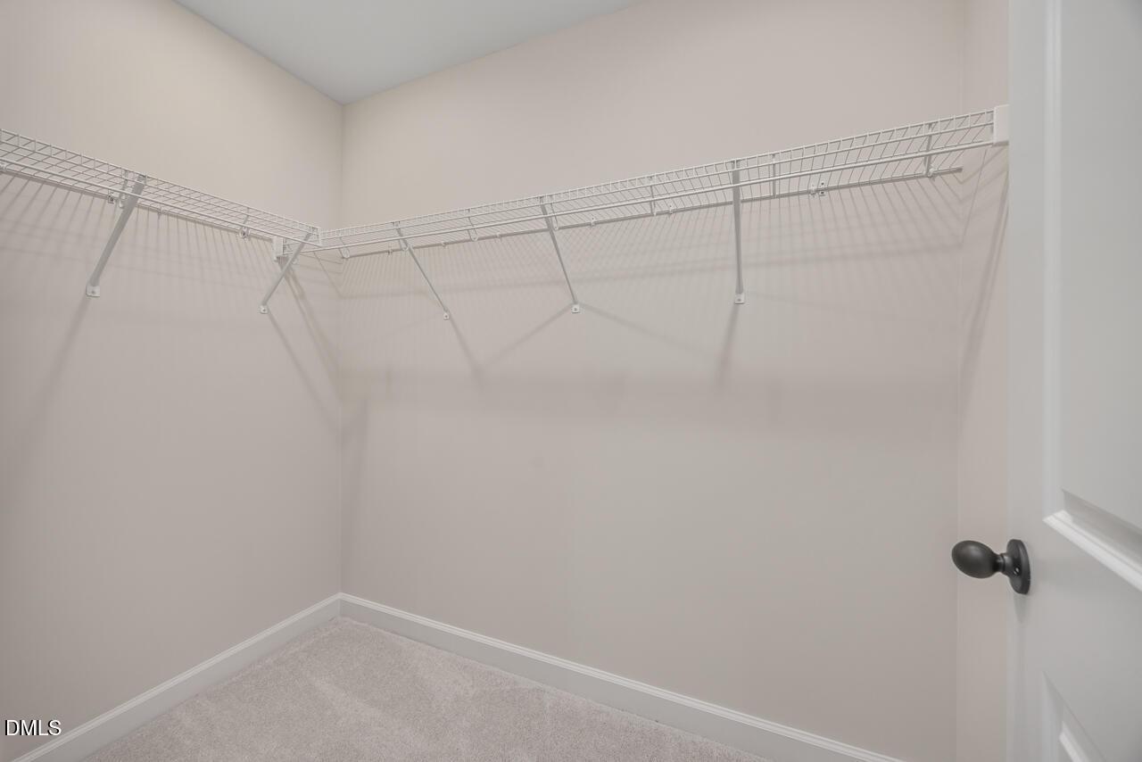 Spacious walk-in closet featuring white wire shelving on beige walls and carpeted floor in Davidson Homes The Mitchell, Knightdale, NC