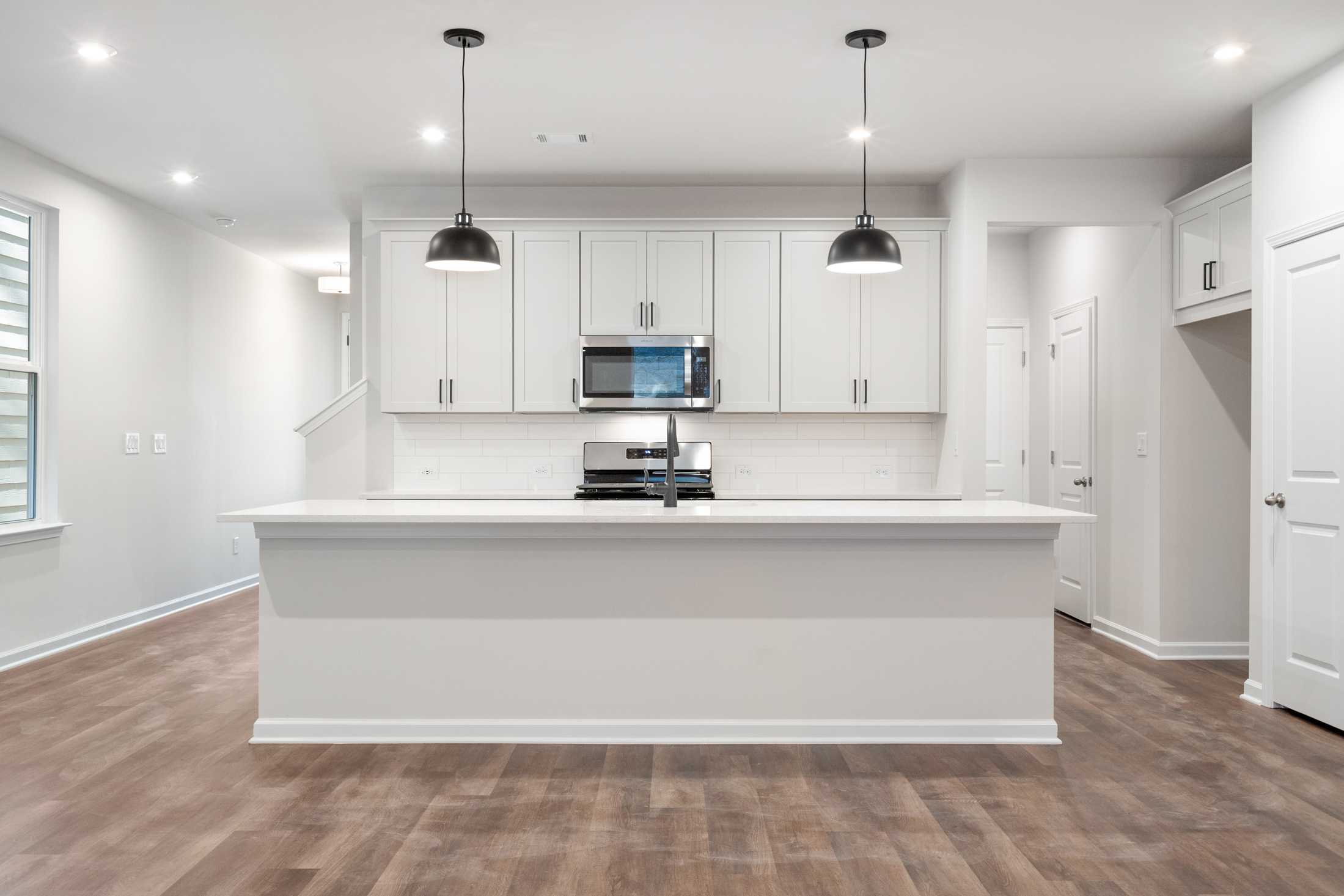 Modern white kitchen in The Cary B by Davidson Homes featuring large island, stainless appliances, and pendant lights