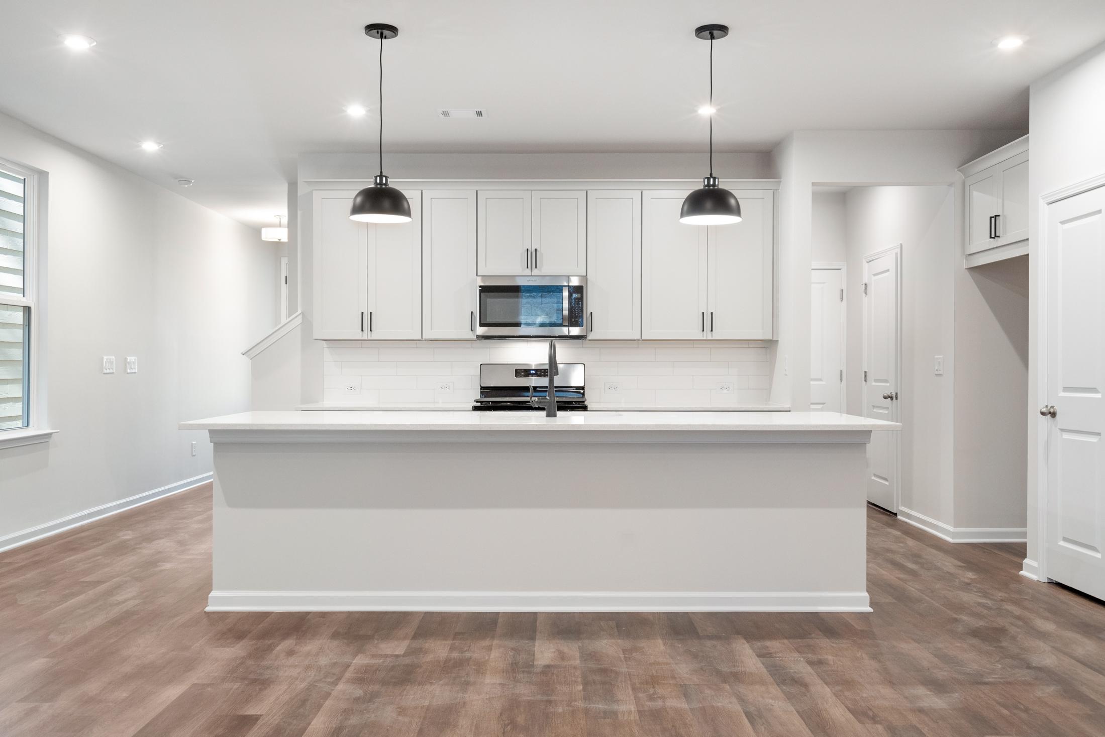 Modern white kitchen in The Cary B by Davidson Homes featuring large island, stainless appliances, and pendant lights