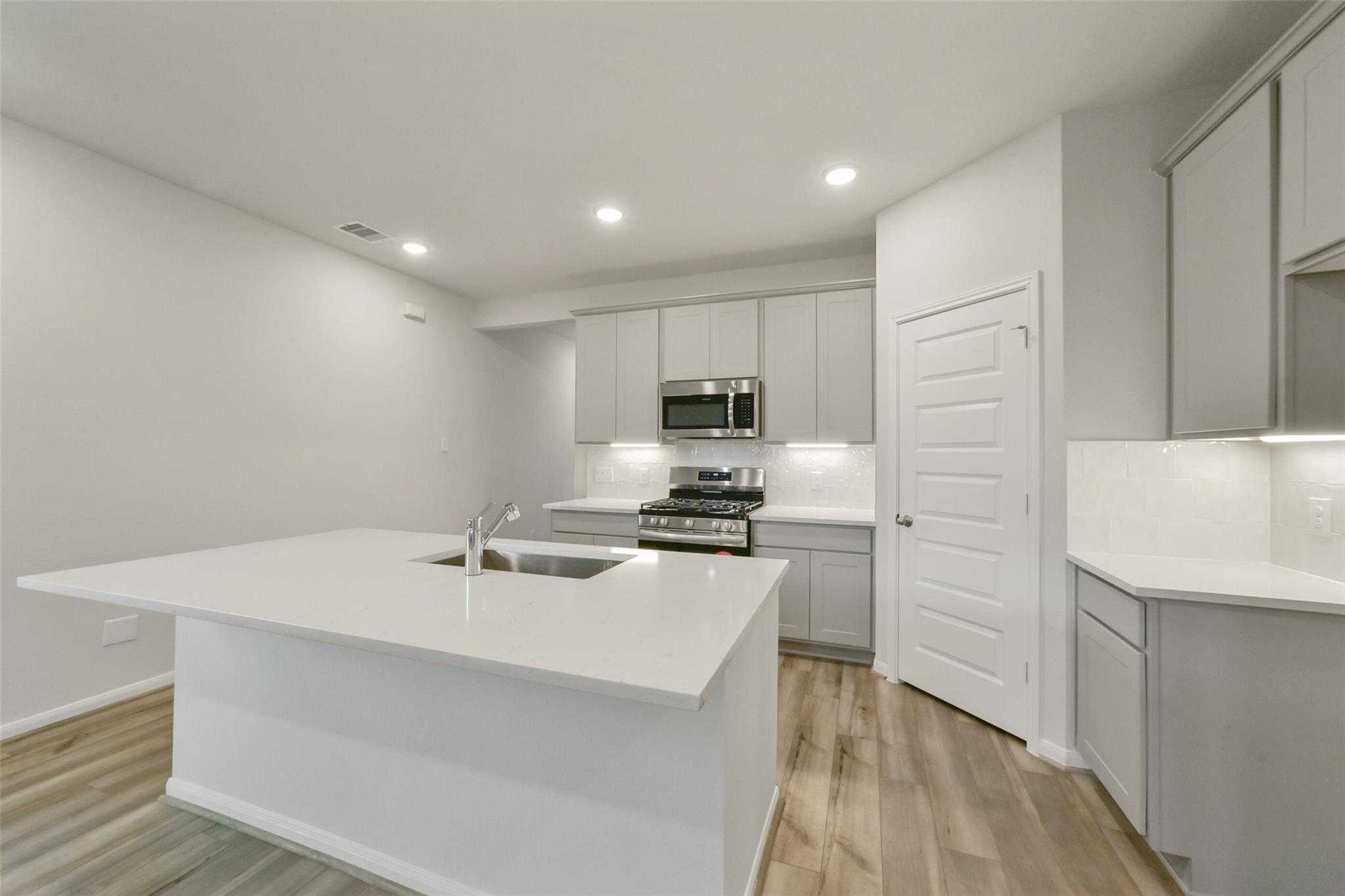 Modern white kitchen with island sink, stainless gas range, recessed lighting in Davidson Homes The San Marcos E, Beasley, TX