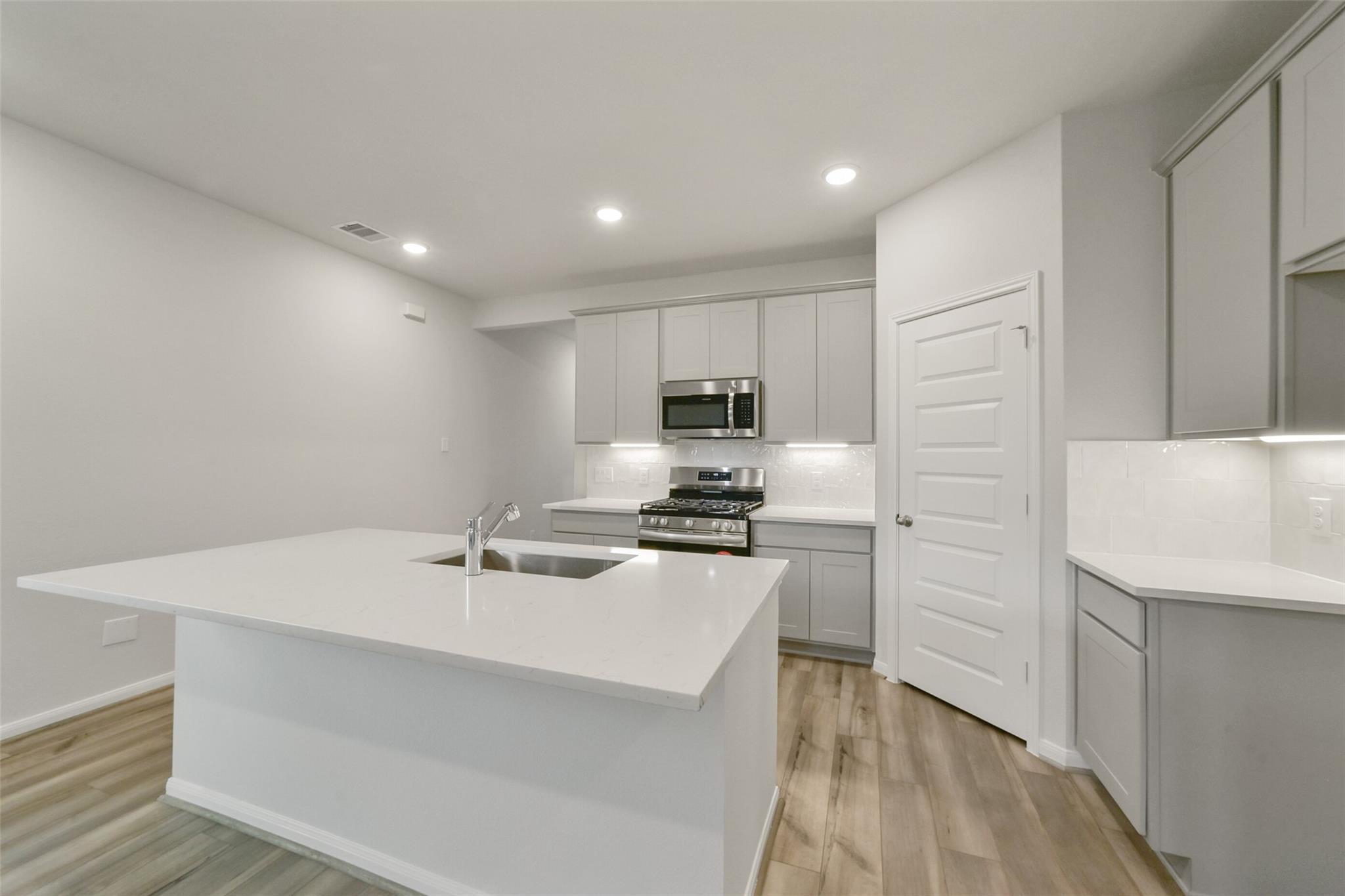 Bright modern kitchen with white shaker cabinets, quartz island sink, stainless appliances in San Marcos E home, Beasley TX