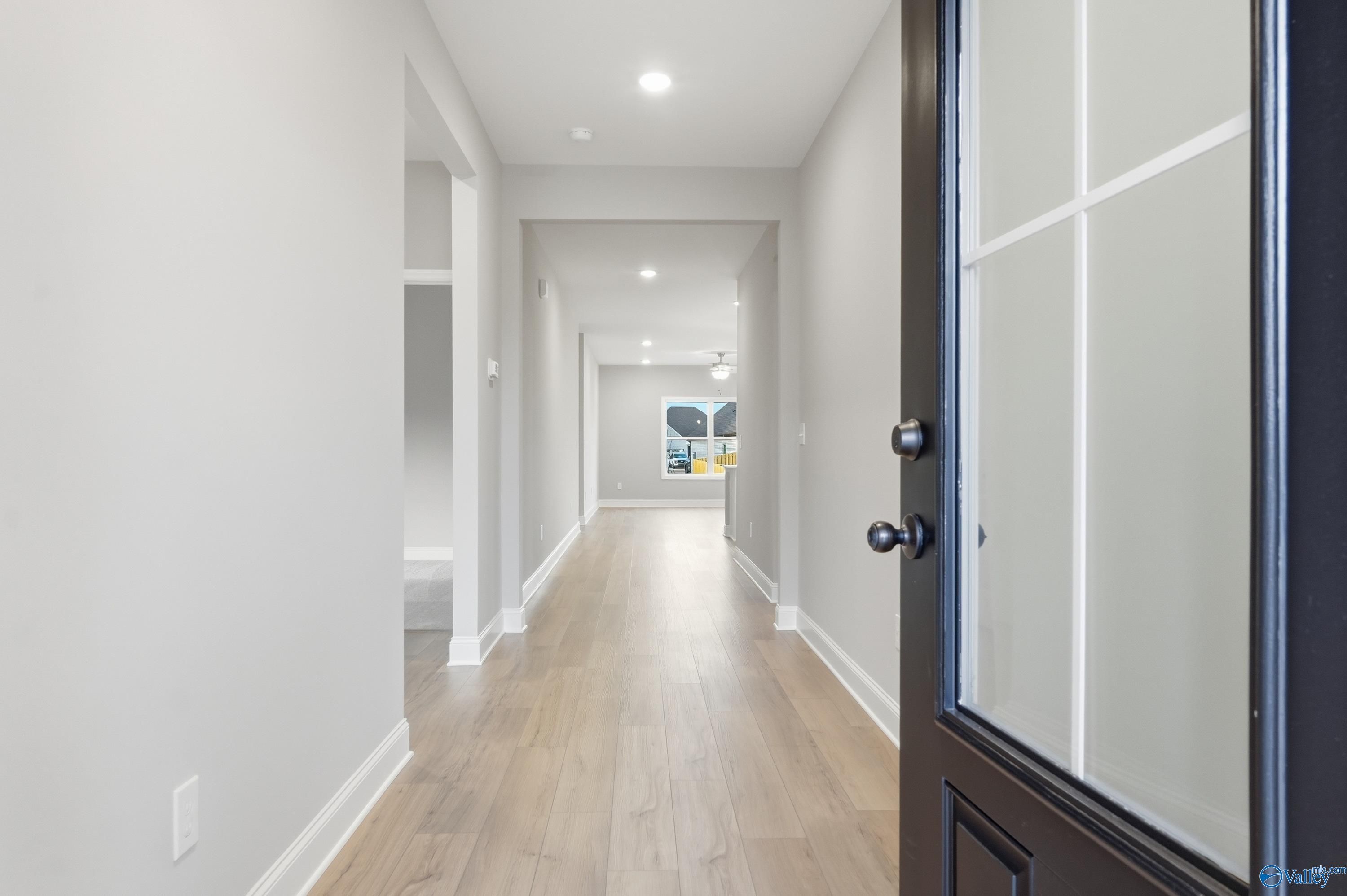 Bright hallway with light oak hardwood floors, white walls, recessed lighting, and frosted glass front door in Davidson Homes The Daphne C, Harvest, AL
