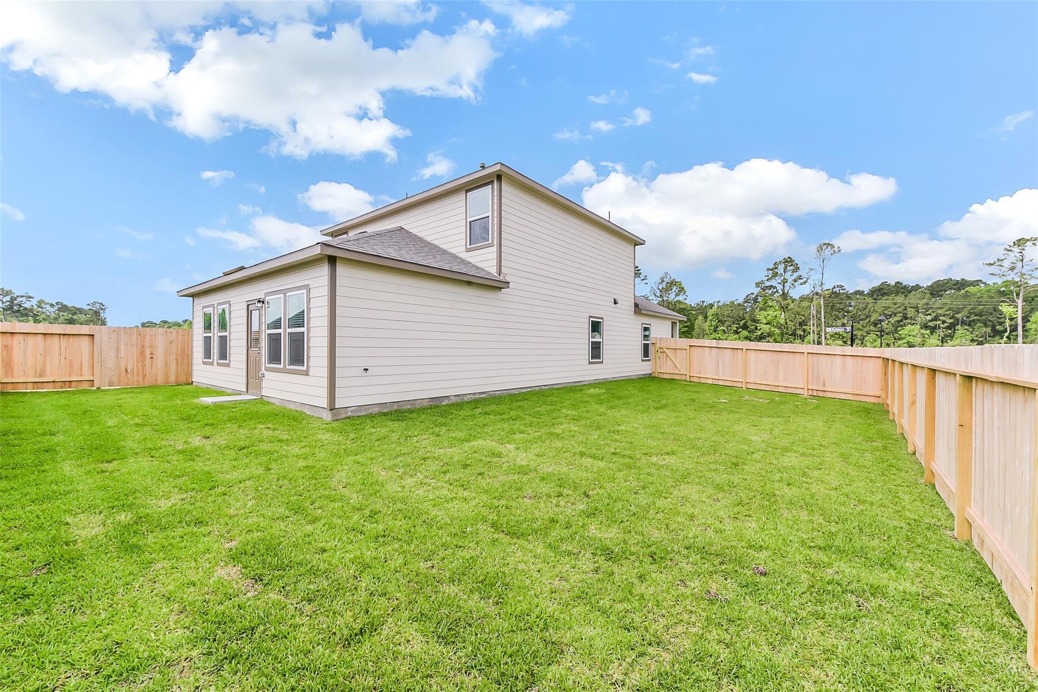 Two-story Sabine F home with beige siding, garage, lush green yard, wooden privacy fence, and wooded backdrop in Dayton, Texas