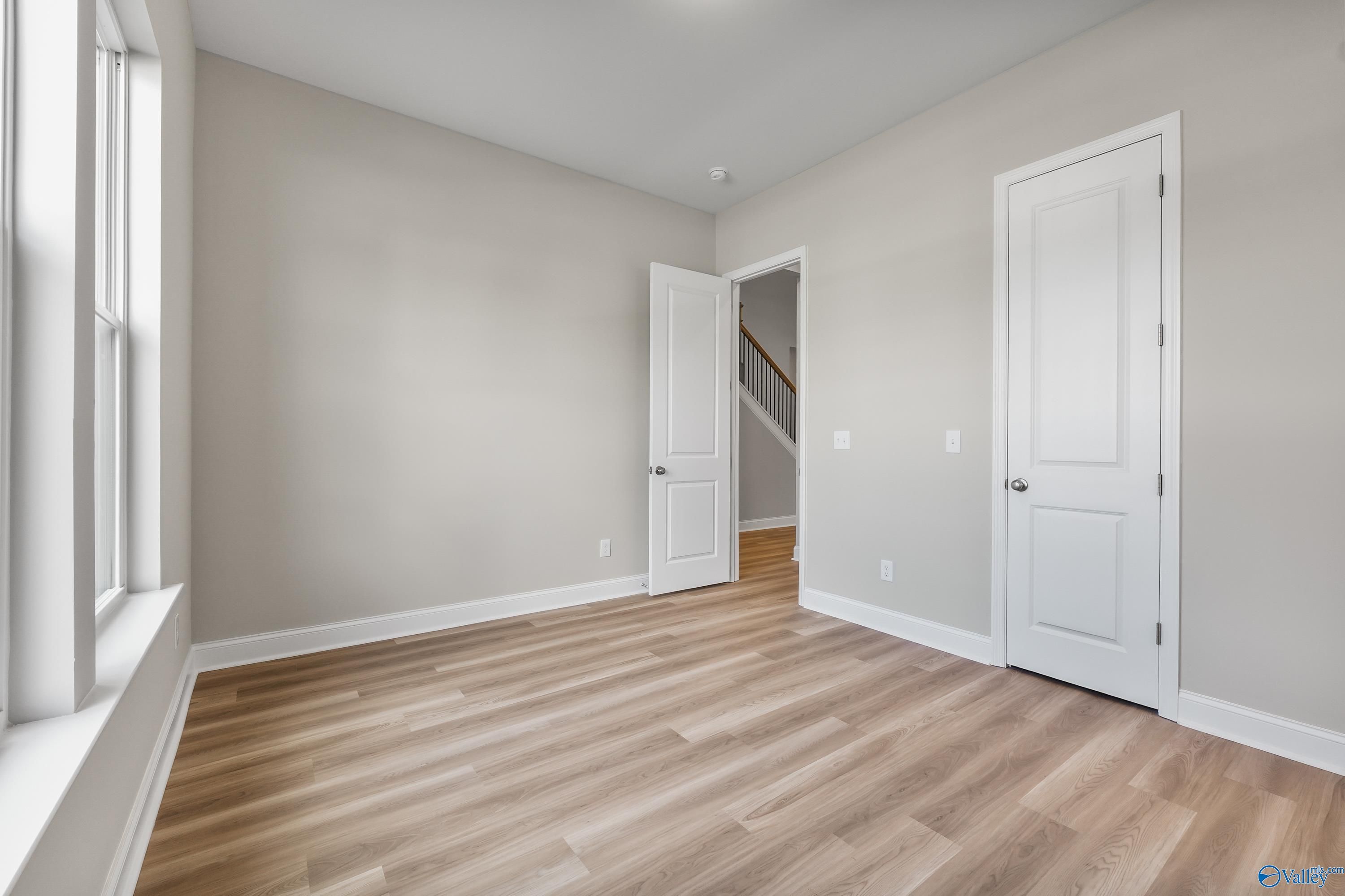 Bright secondary bedroom with beige walls, hardwood floors, and double windows in Evermore Homes The Haven, Owens Cross Roads, Alabama