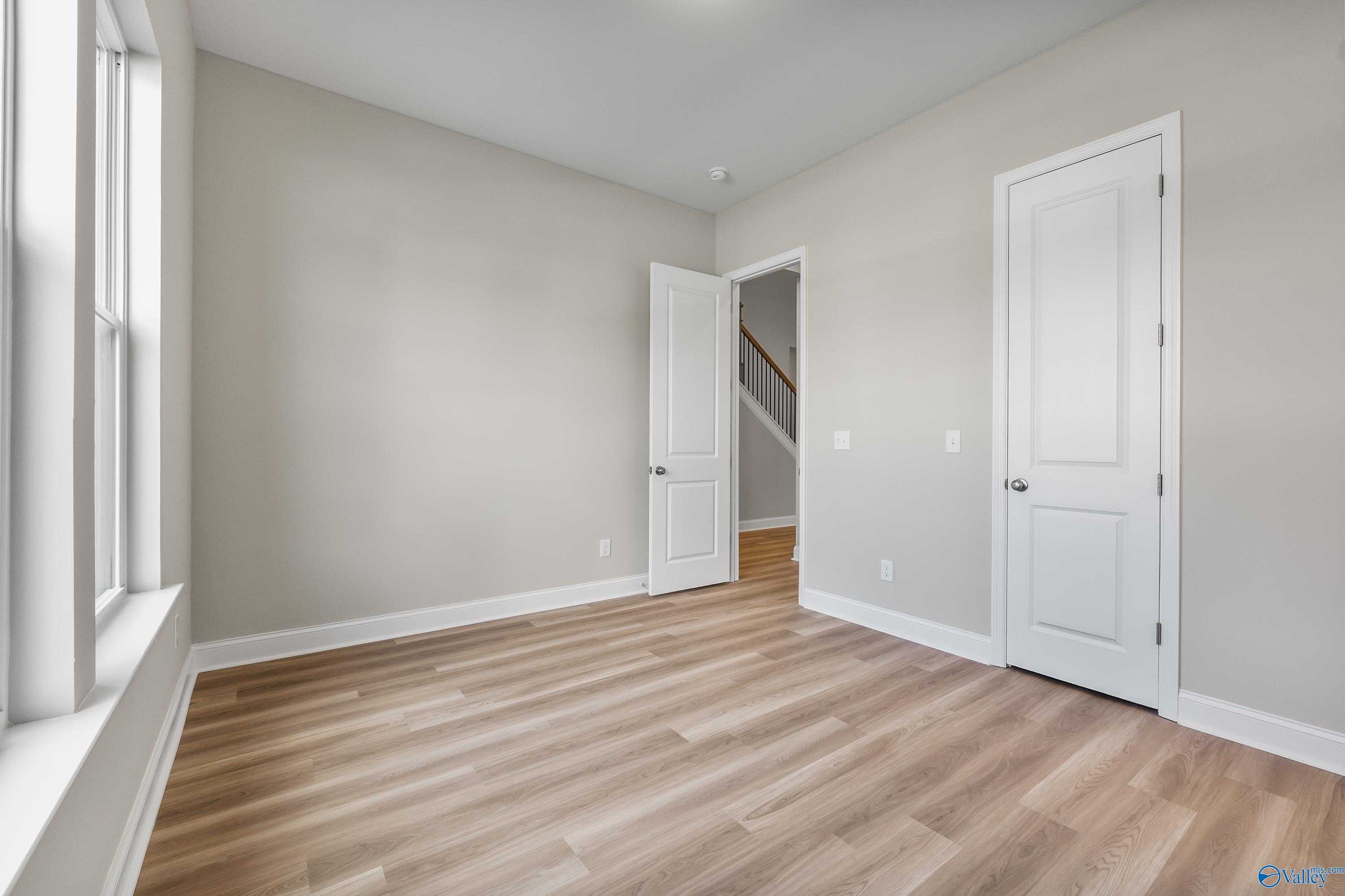 Bright secondary bedroom with beige walls, hardwood floors, and double windows in Evermore Homes The Haven, Owens Cross Roads, Alabama