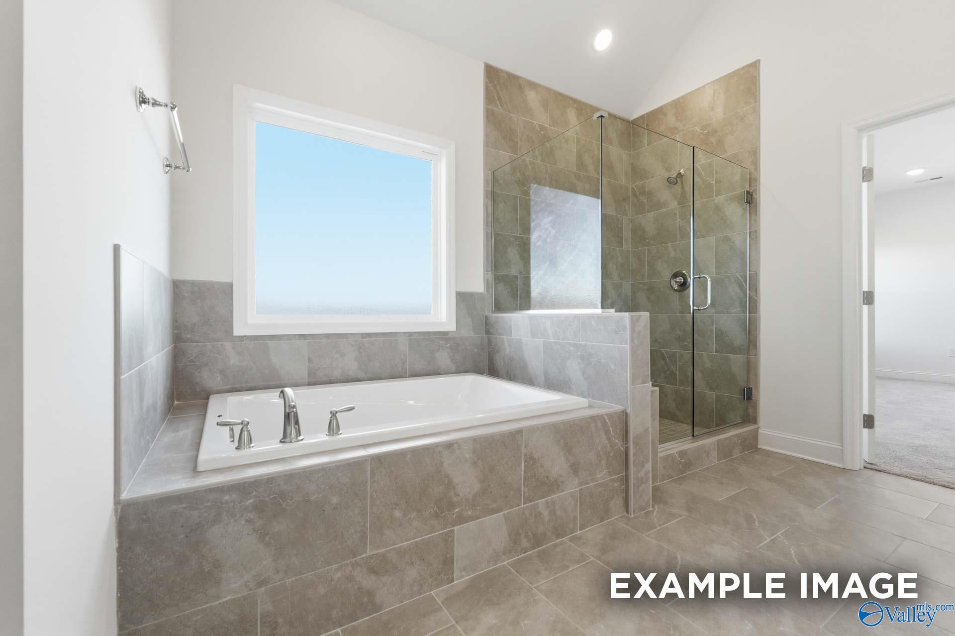 Modern primary bathroom with tiled soaking tub and glass-enclosed shower in The Valencia floor plan, Briercreek, AL.