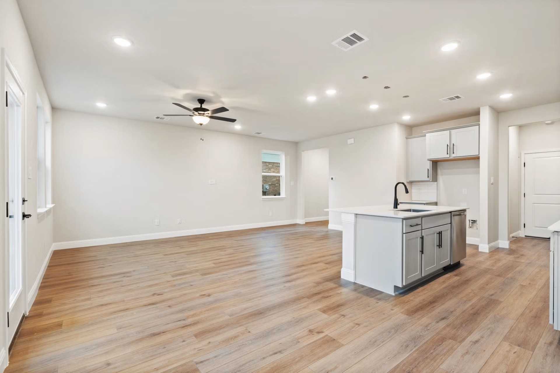 Open-concept living room and kitchen with hardwood floors, gray island sink, and ceiling fan in Davidson Homes The Wake D, Wylie, Texas