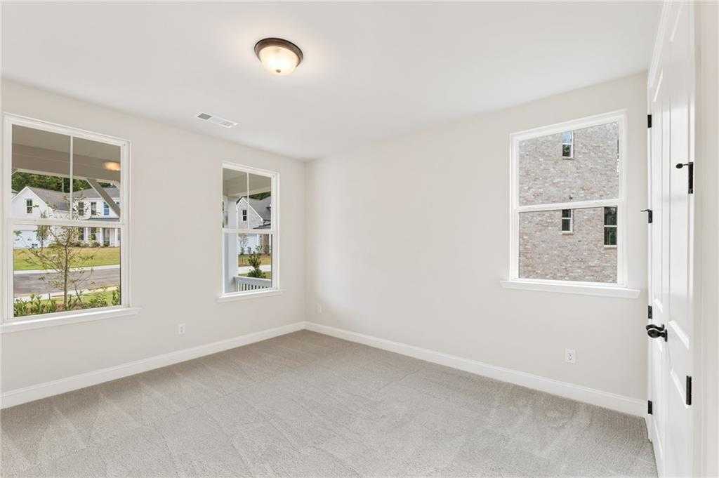 Spacious secondary bedroom with neutral walls, gray carpet, and large windows overlooking neighborhood in The Hickory B, Buford, GA