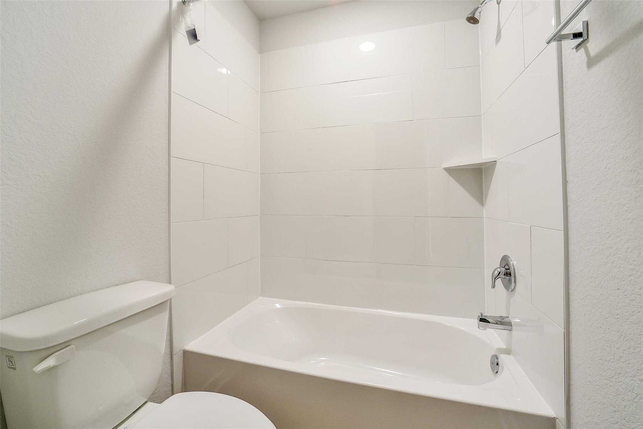 Bright white tiled bathroom with soaking tub, walk-in shower, and toilet in Davidson Homes The Trinity F, Magnolia, Texas